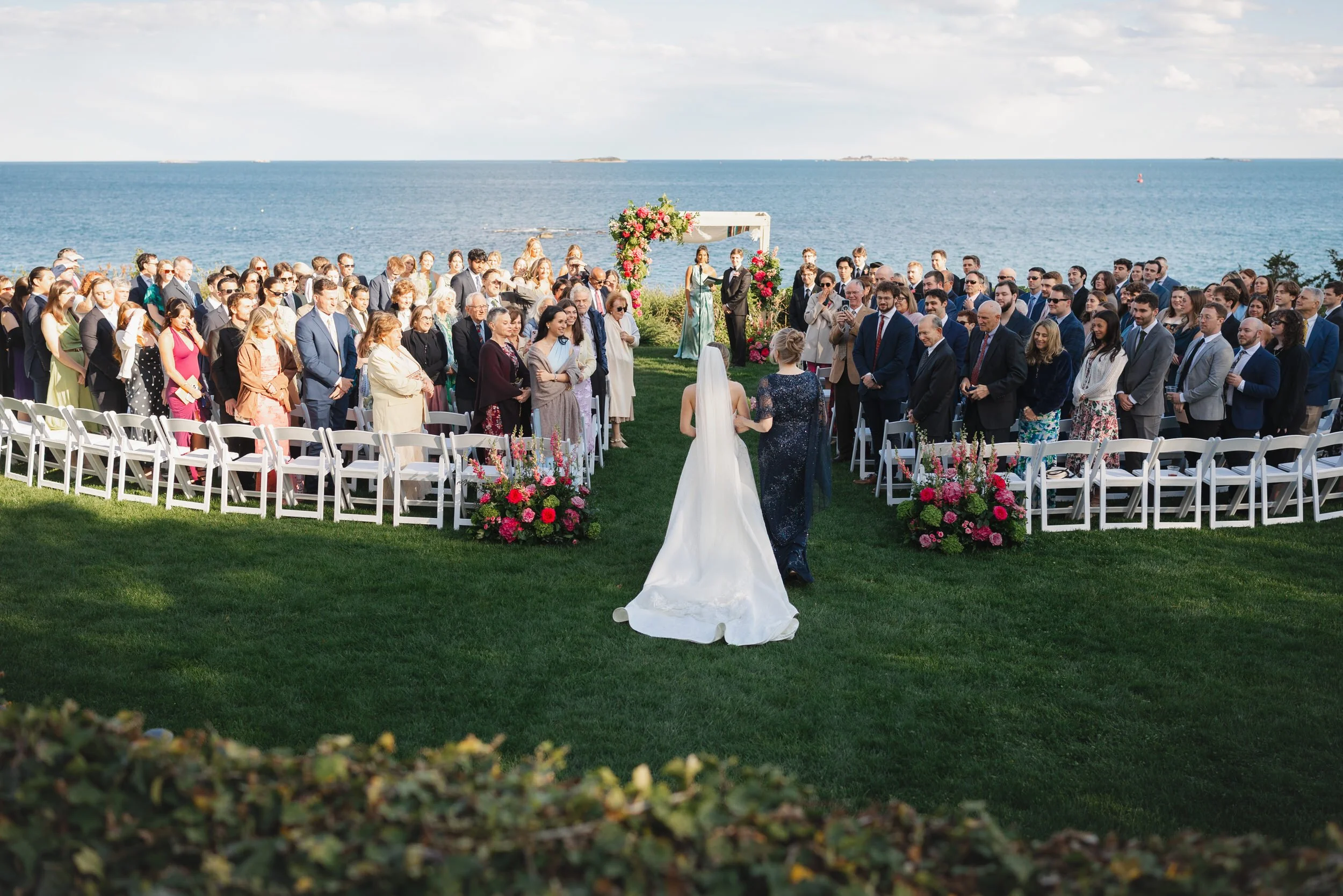 Modern oceanfront wedding ceremony with pink, mauve, and green florals