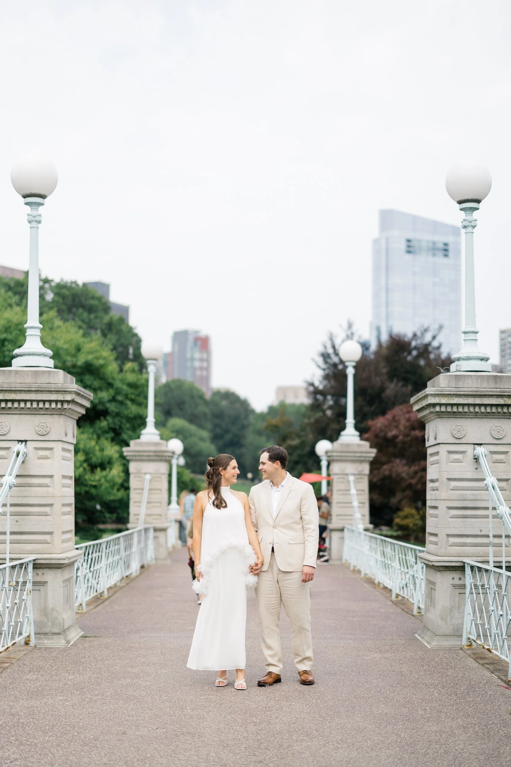 Couple strolling through the Boston Public Garden beneath lush summer trees.