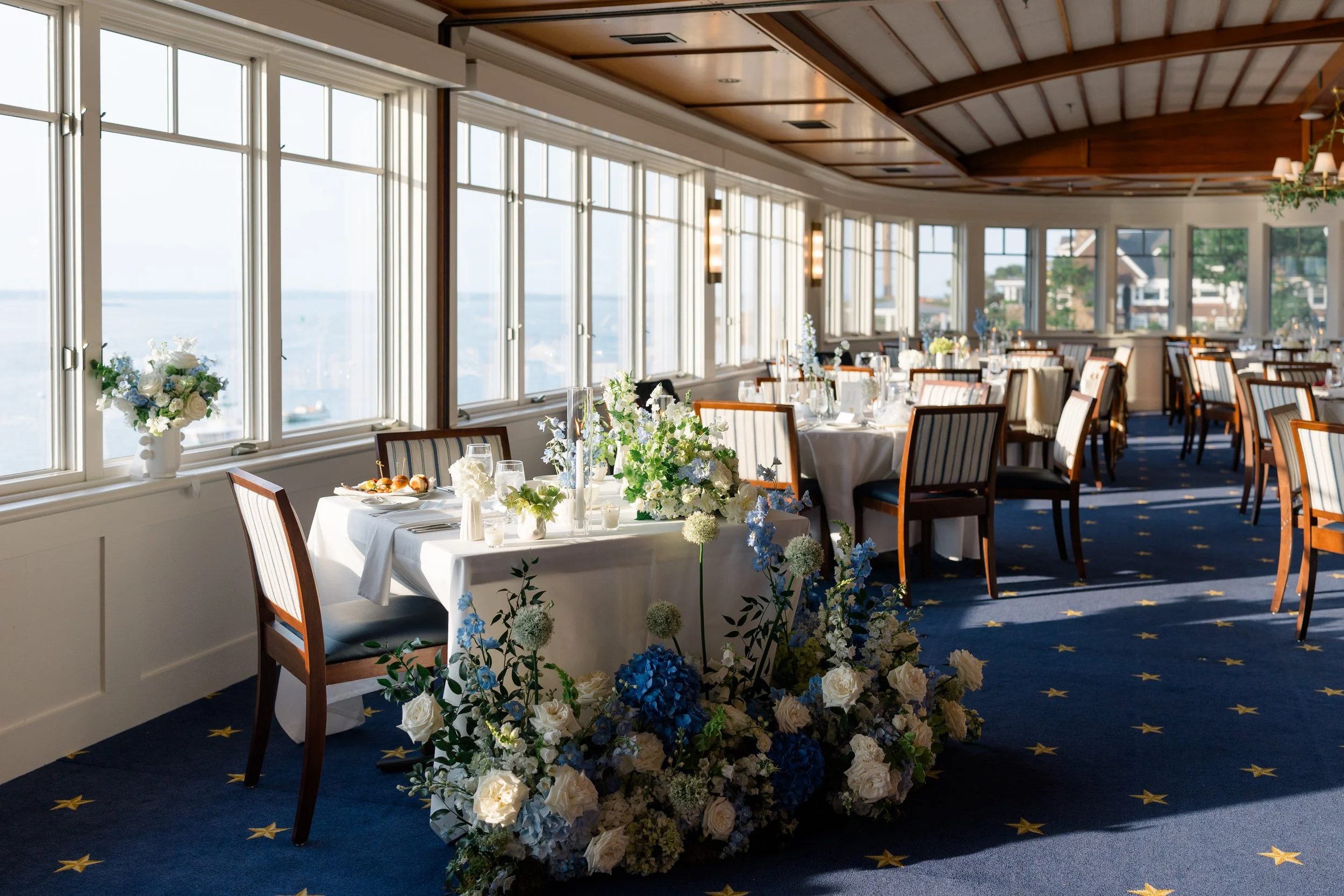 Reception details at Corinthian Yacht Club in Marblehead featuring floral arrangements in handmade ceramic vessels overlooking a sail-filled harbor.