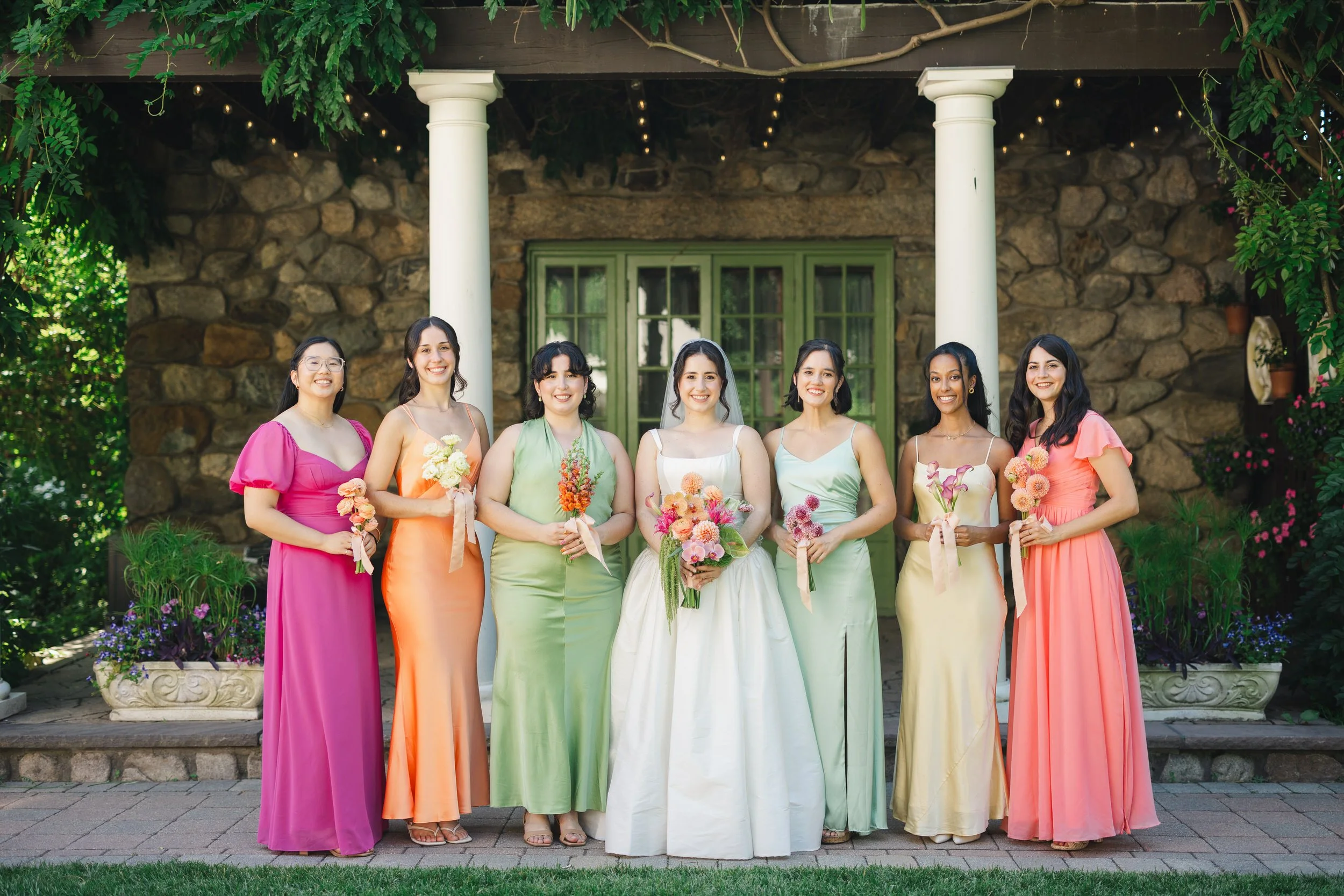 Bridesmaids wearing pink orange green and yellow dresses holding unique monochromatic bouquets at Willowdale Estate wedding