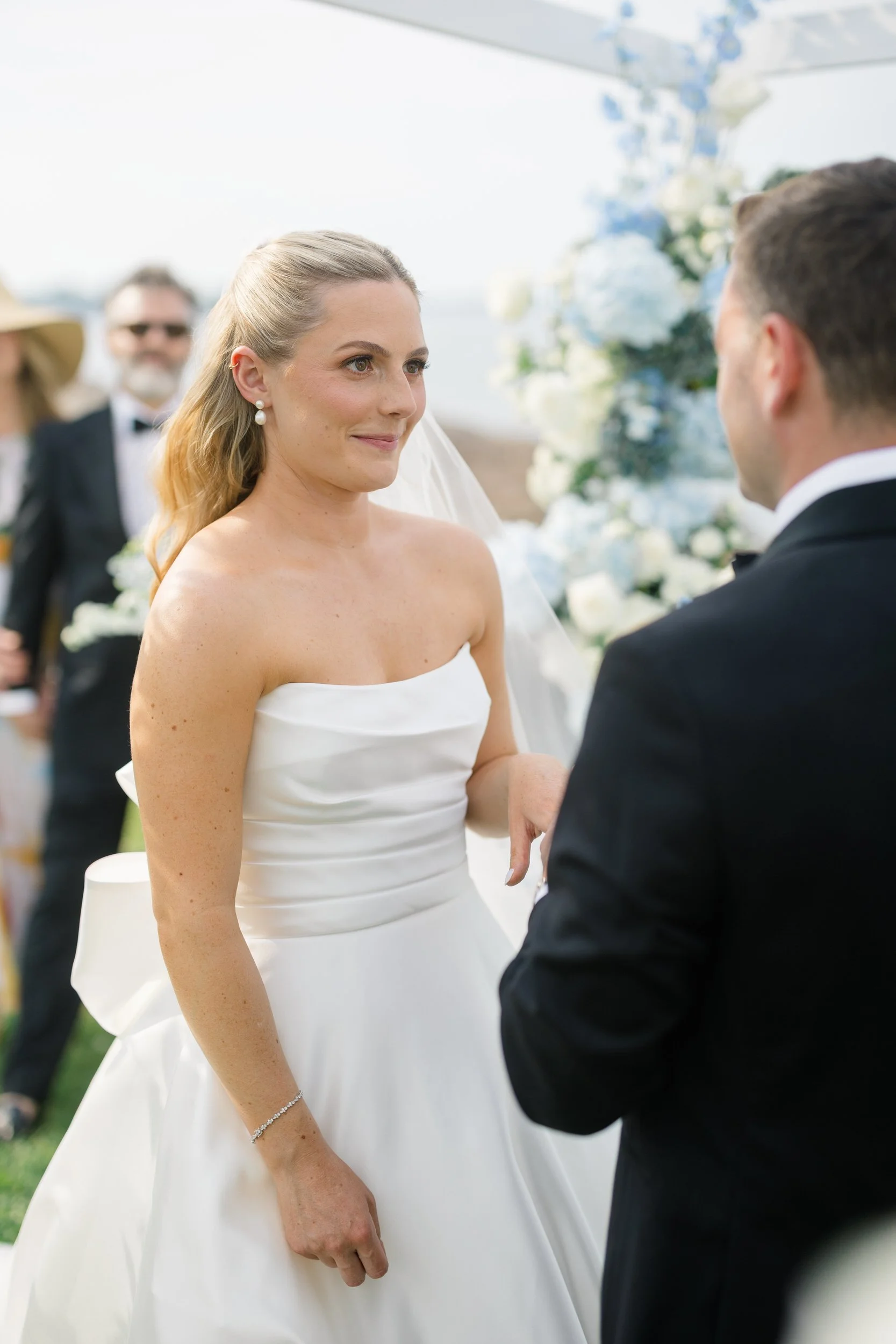 Bride and groom exchanging vows during a waterfront ceremony in Marblehead, Massachusetts with sailboats in the background.