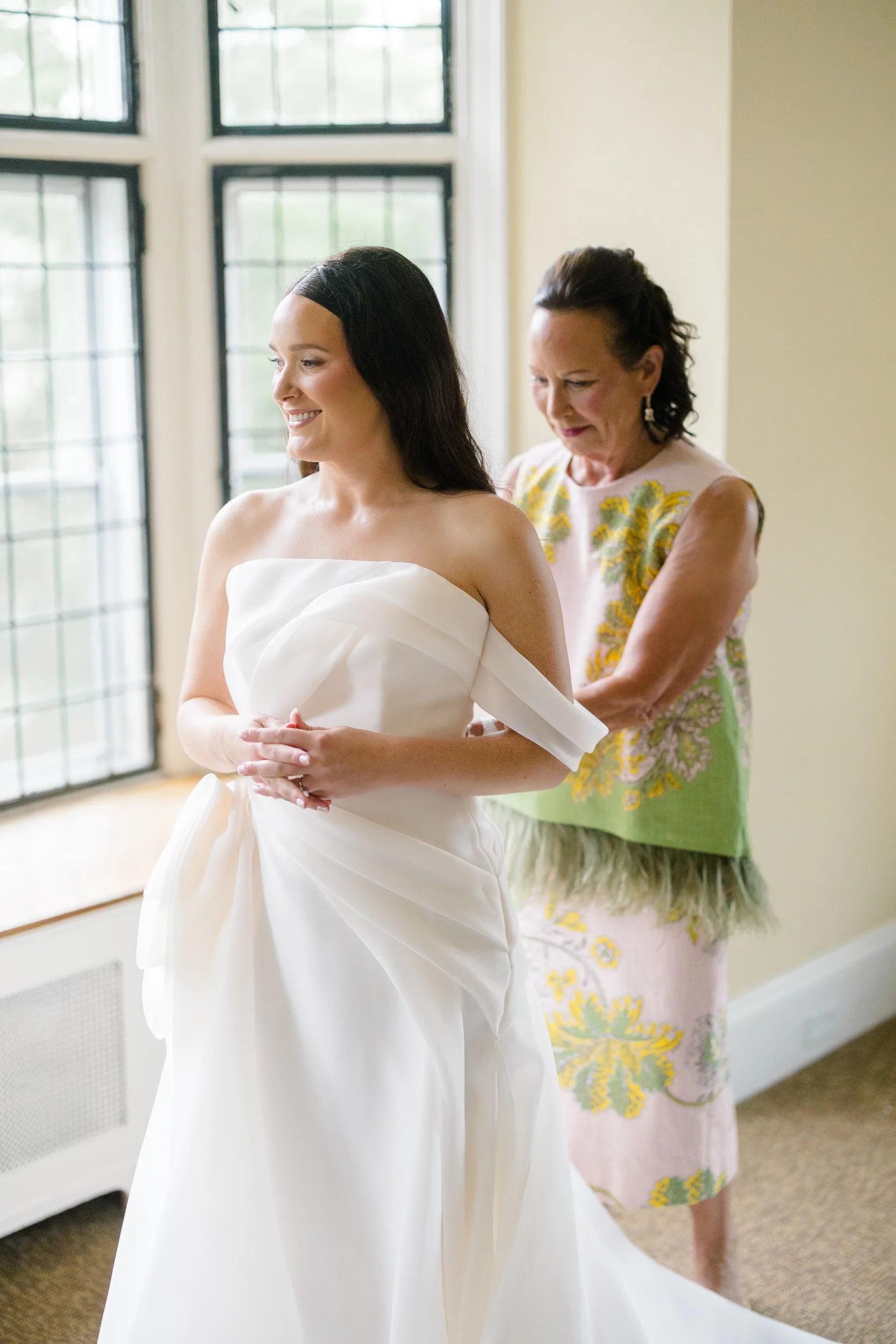 Bride putting on her gown as colorful pink, orange, yellow, and red flowers fill the getting-ready space.