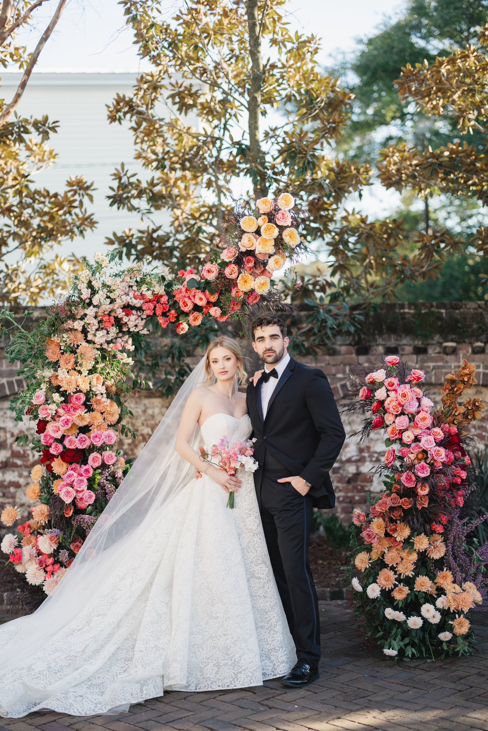 Newlyweds embracing beneath pink climbing florals at The Gadsen House