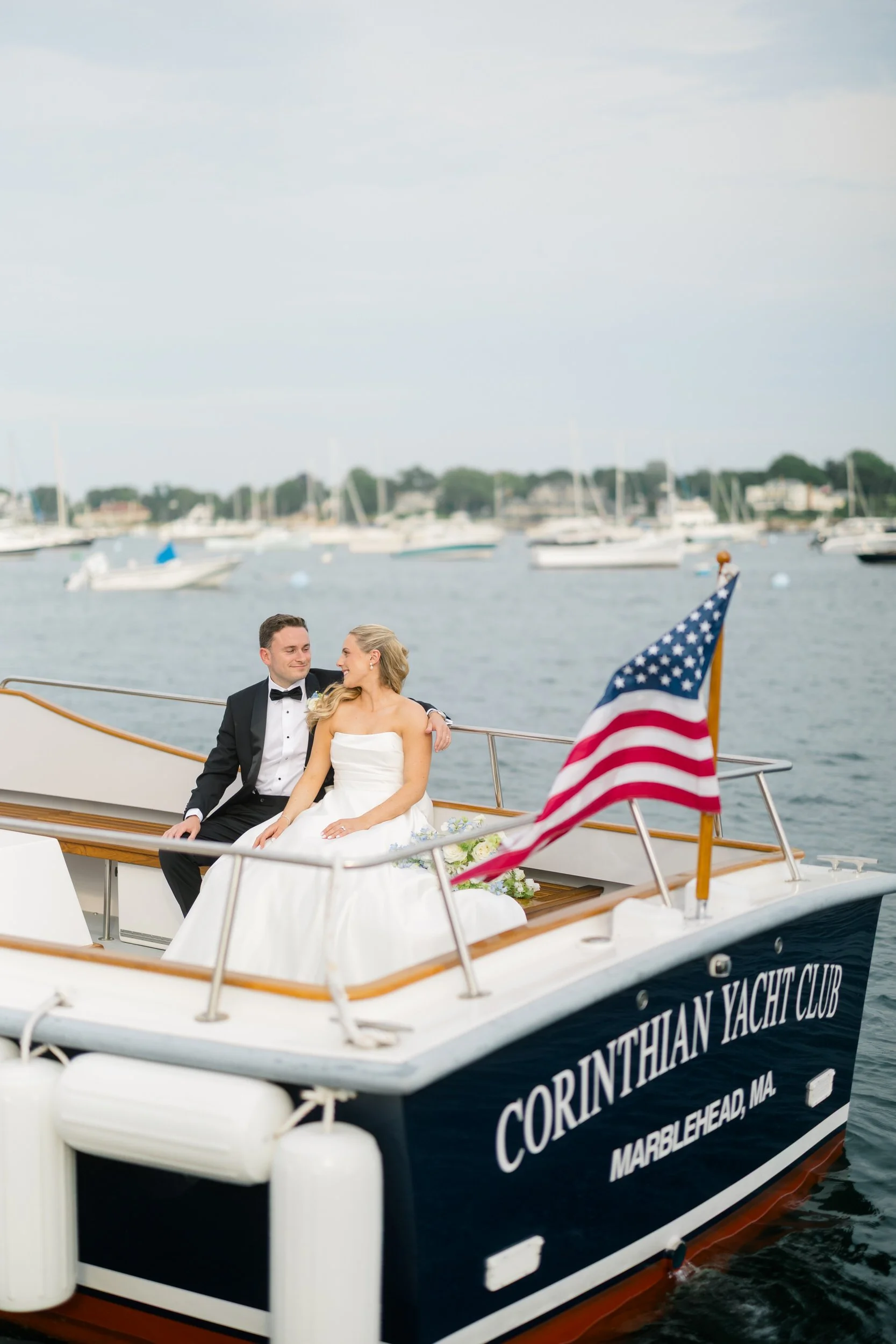 Bride and groom boat portraits sailing through Marblehead Harbor during a Corinthian Yacht Club wedding with hundreds of sailboats in the background.