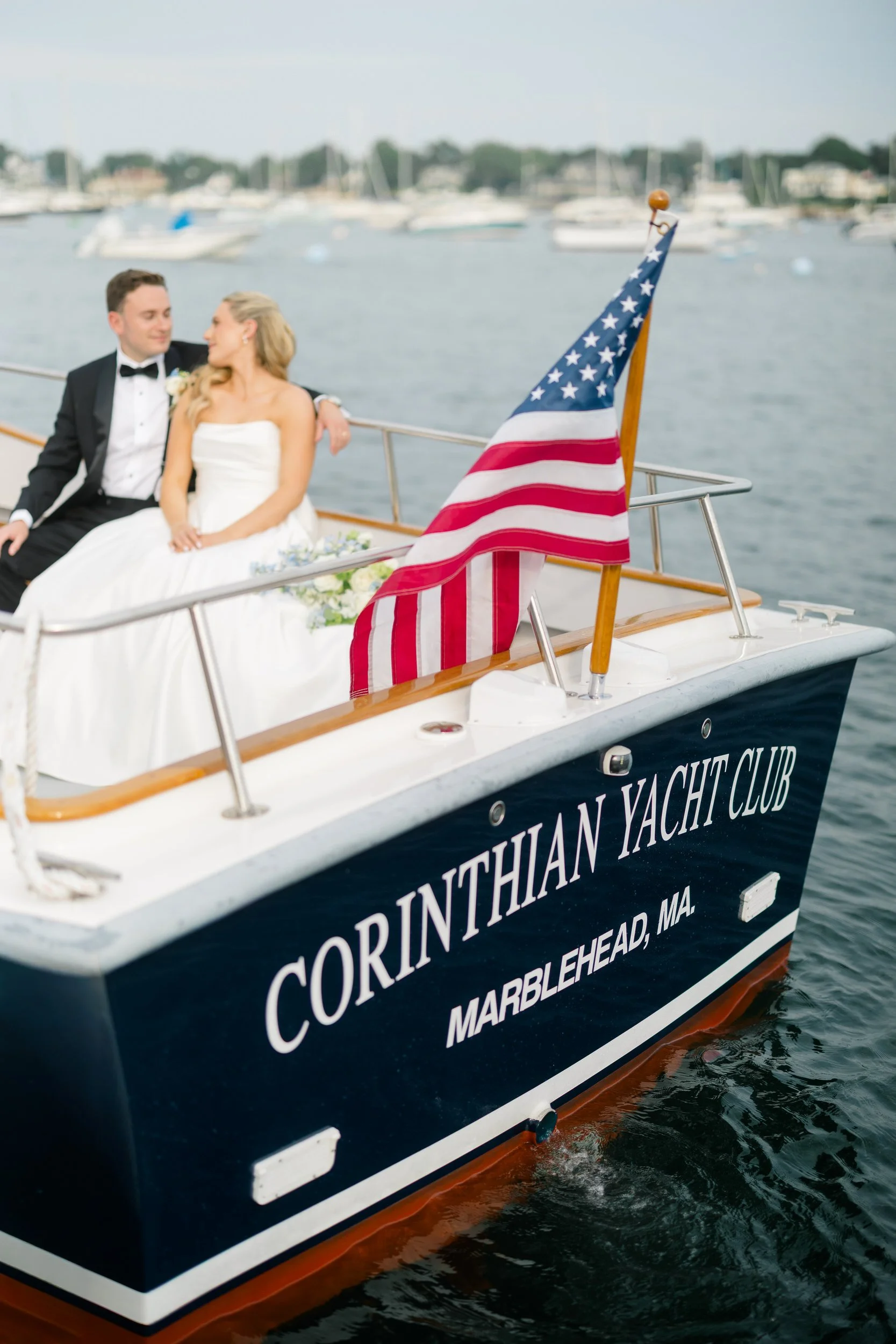 Bride and groom boat portraits sailing through Marblehead Harbor during a Corinthian Yacht Club wedding with hundreds of sailboats in the background.