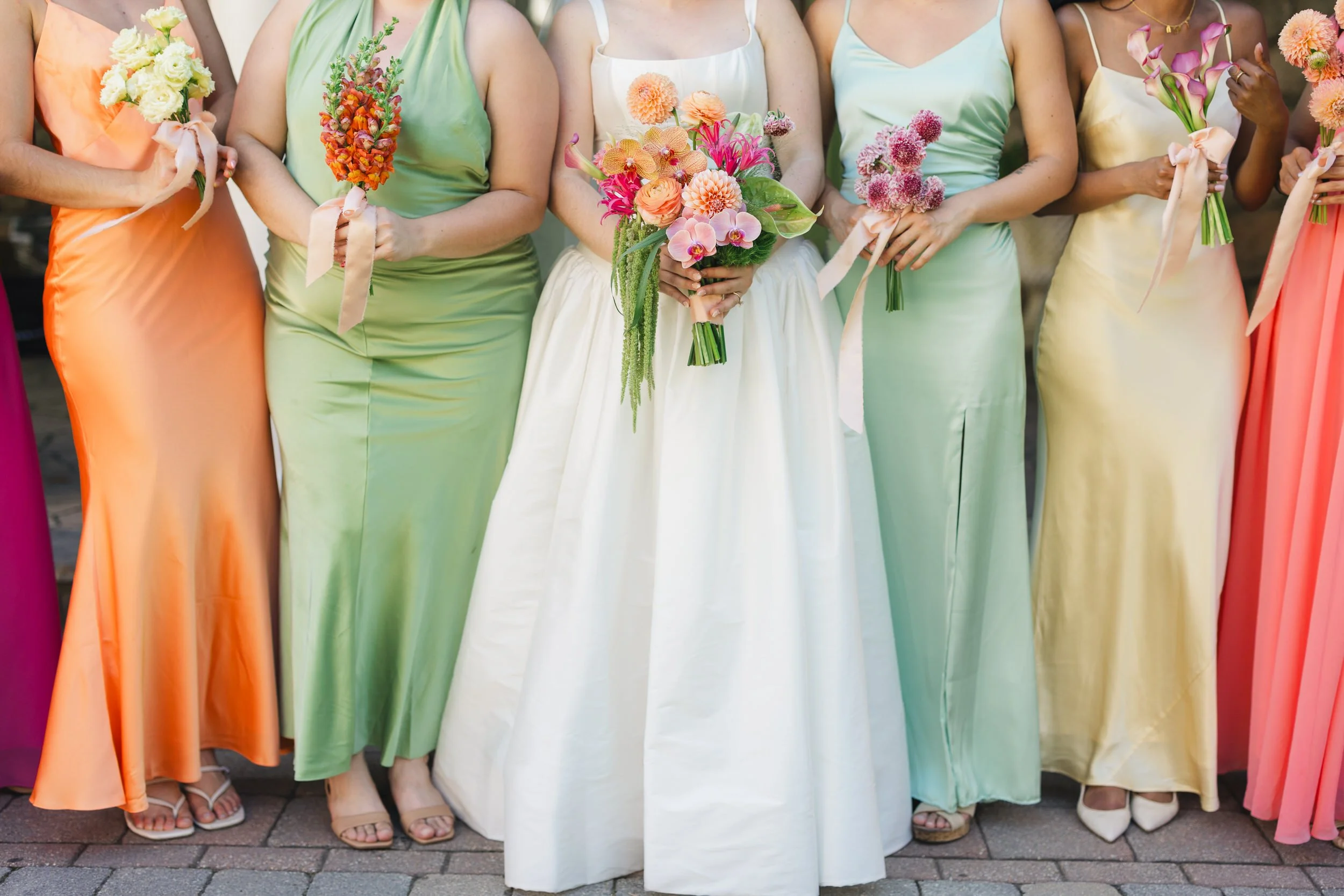 Bridesmaids in mismatched bright dresses holding orchids dahlias and ranunculus at Willowdale Estate