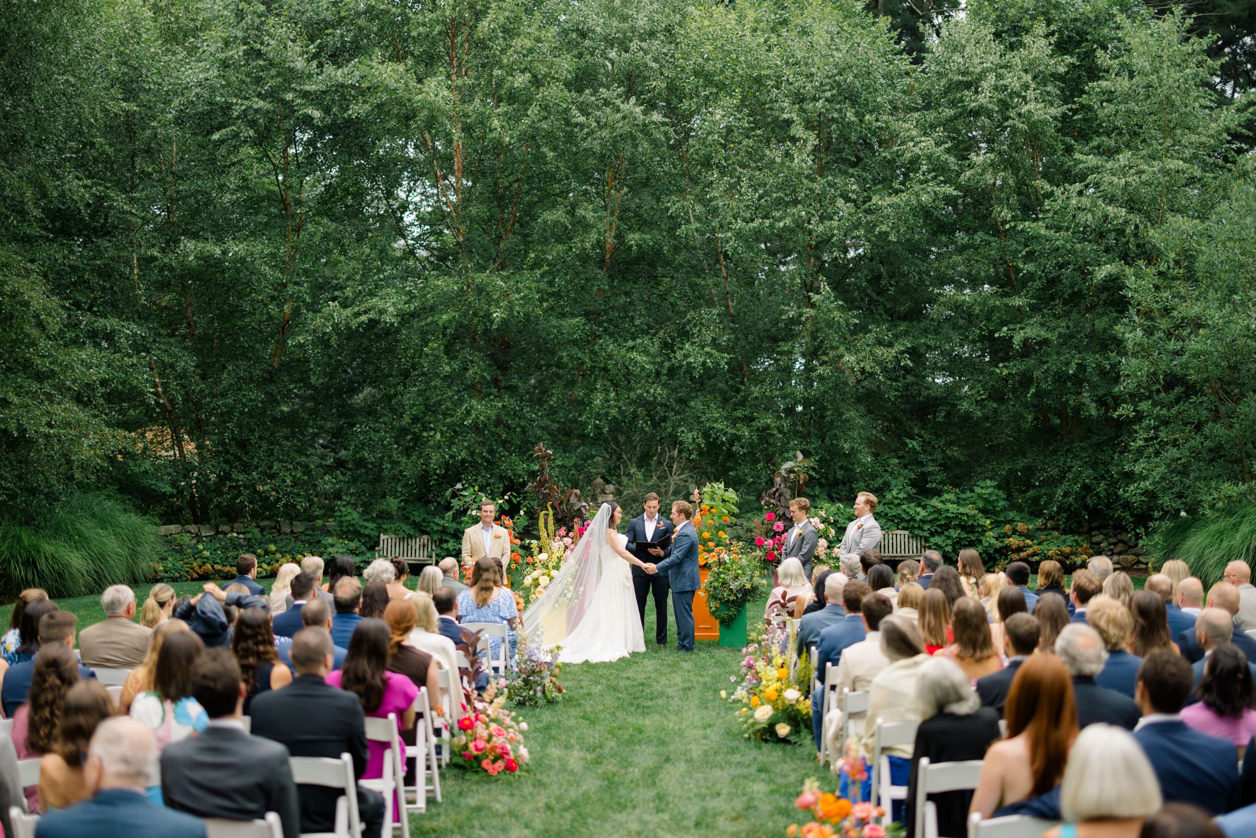 Couple exchanging vows surrounded by bright dahlias, English roses, and poppies.