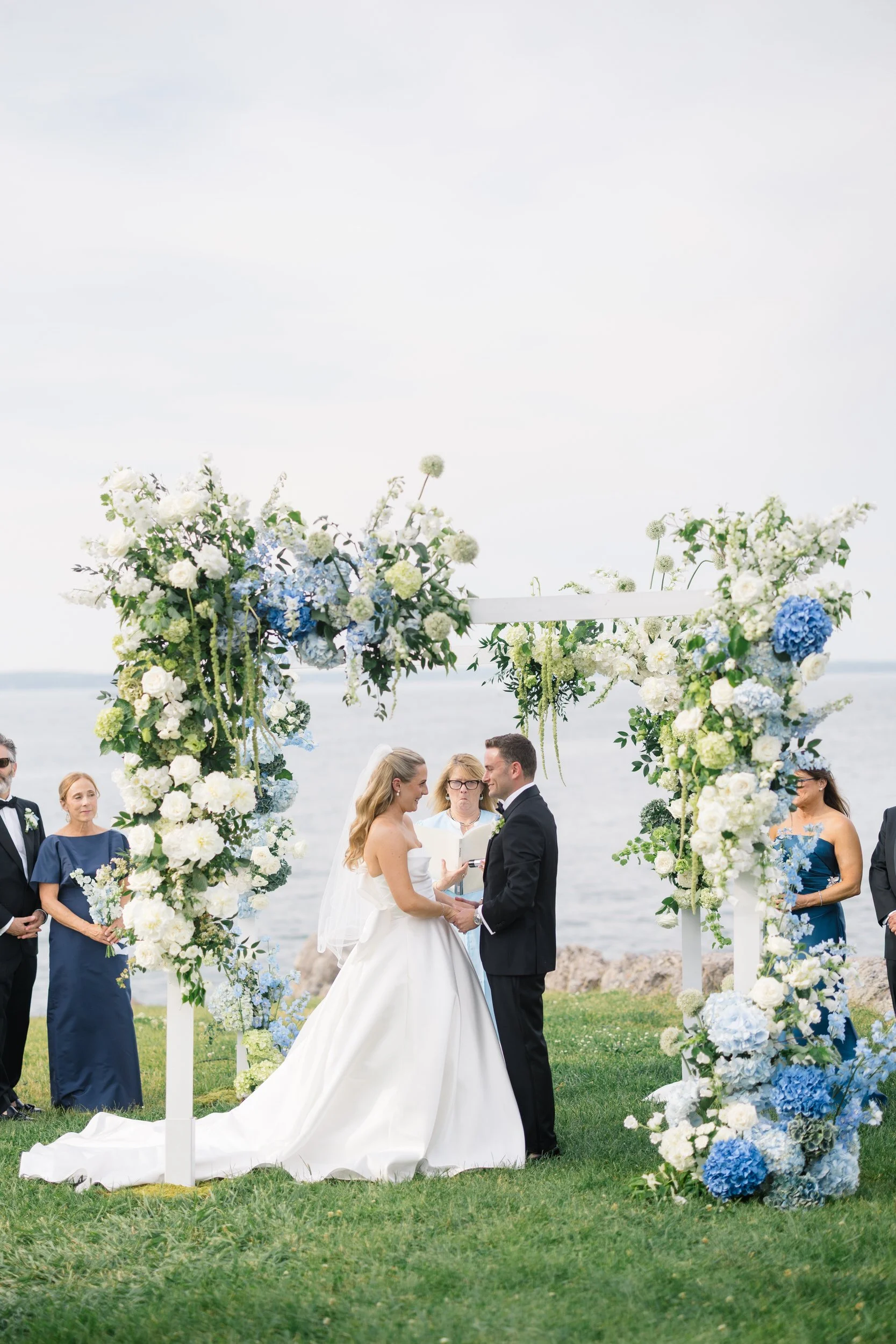 Bride and groom exchanging vows during a waterfront ceremony in Marblehead, Massachusetts with sailboats in the background.