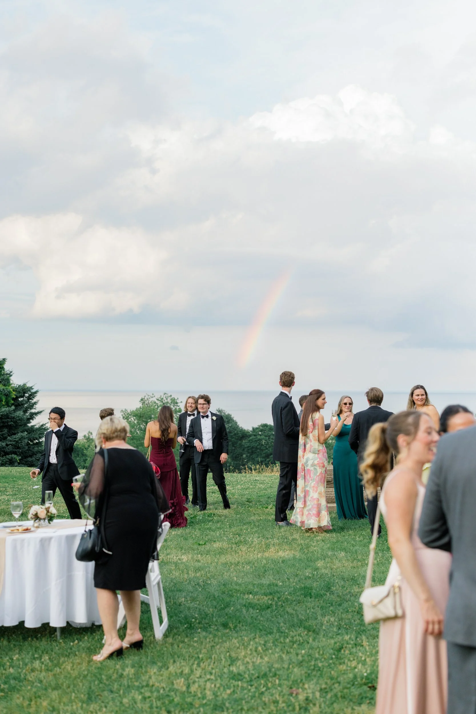 A dramatic rainbow appearing over cocktail hour on the Crane Estate grounds during a summer wedding celebration.