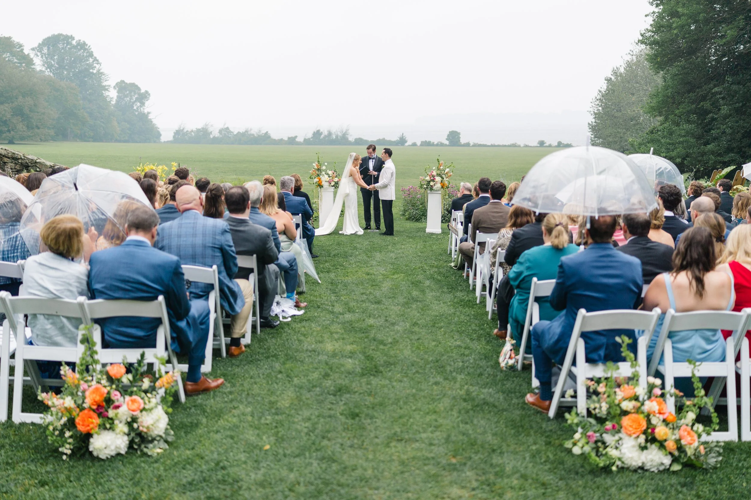 Bride and groom exchanging vows beneath umbrellas during their rainy garden ceremony at Blithewold Mansion & Gardens.