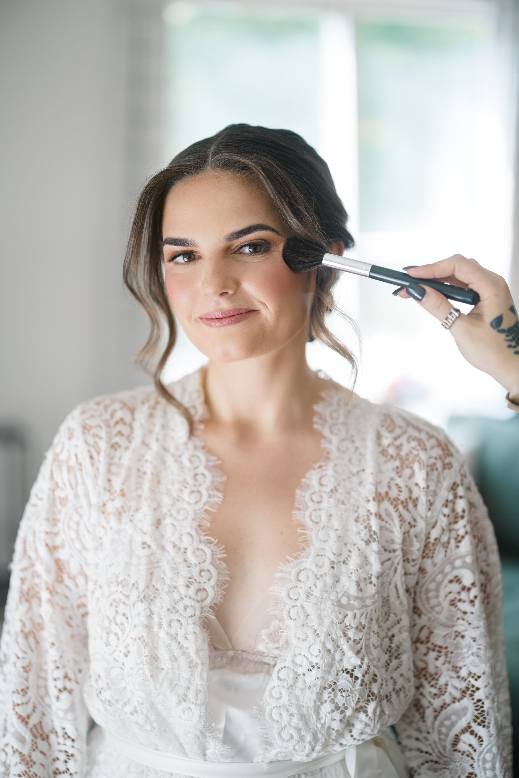 The bride smiling as the finishing touches are added to her hair and makeup before her Crane Estate wedding in Ipswich, Massachusetts.