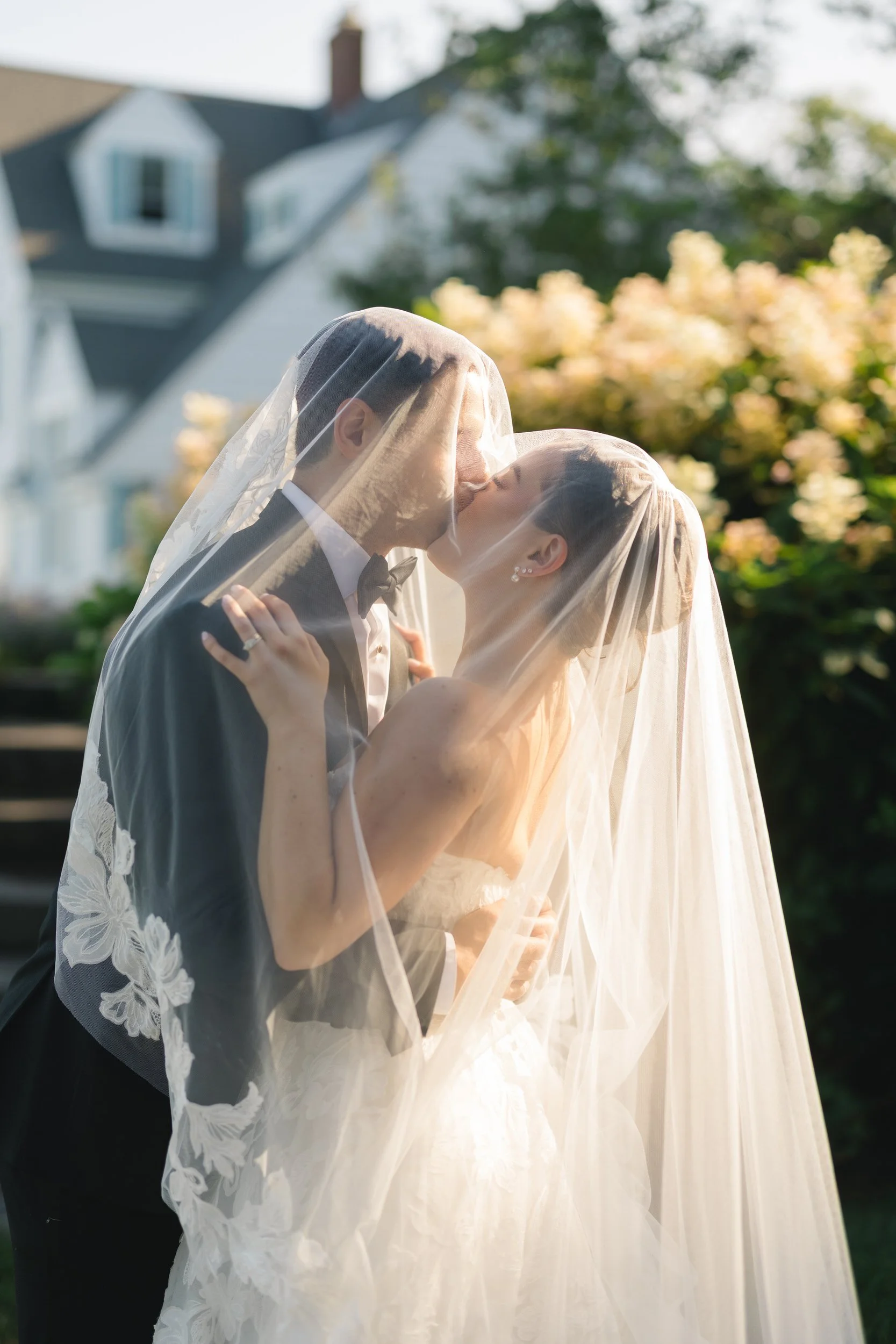 Bride and groom embracing beside lush hydrangeas overlooking the Cape Cod coastline.