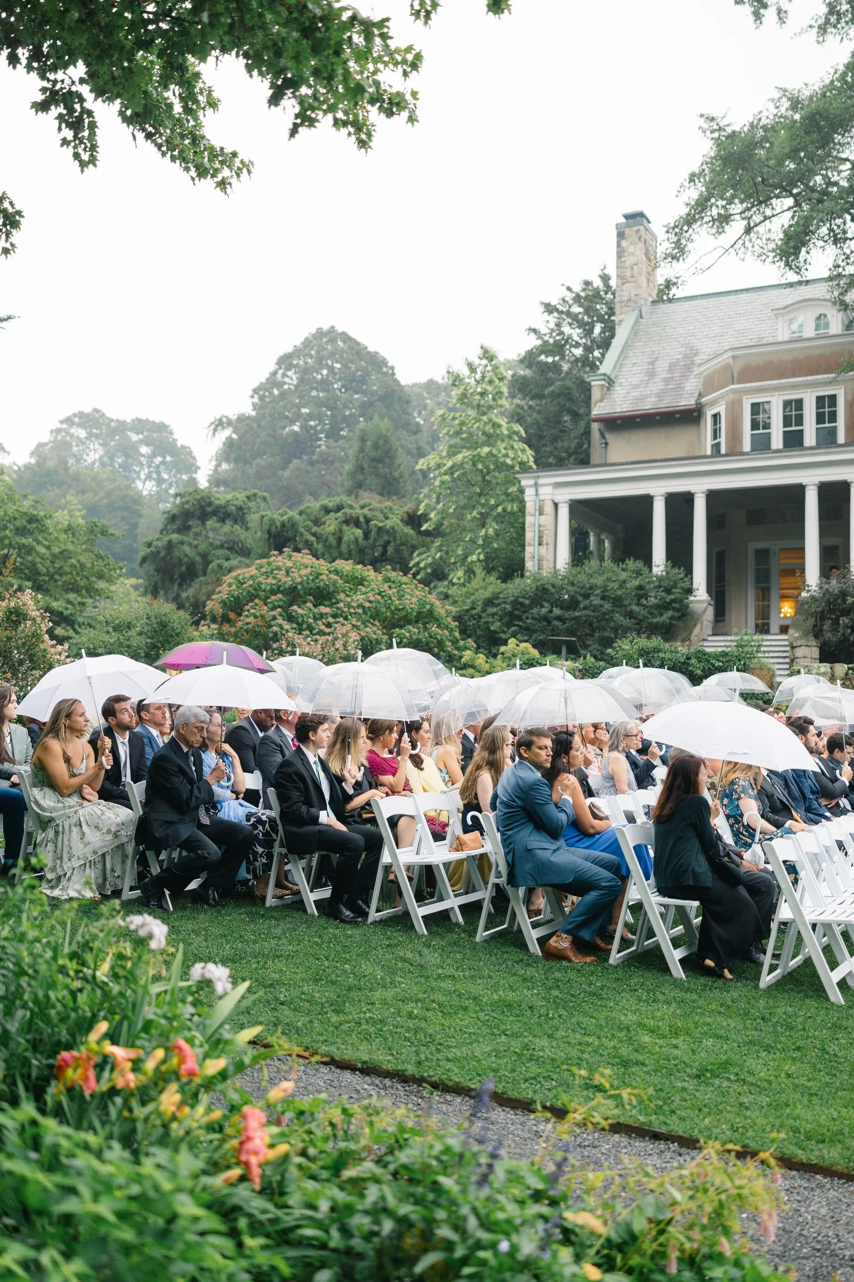 Outdoor wedding ceremony in the gardens at Blithewold with guests holding white umbrellas.