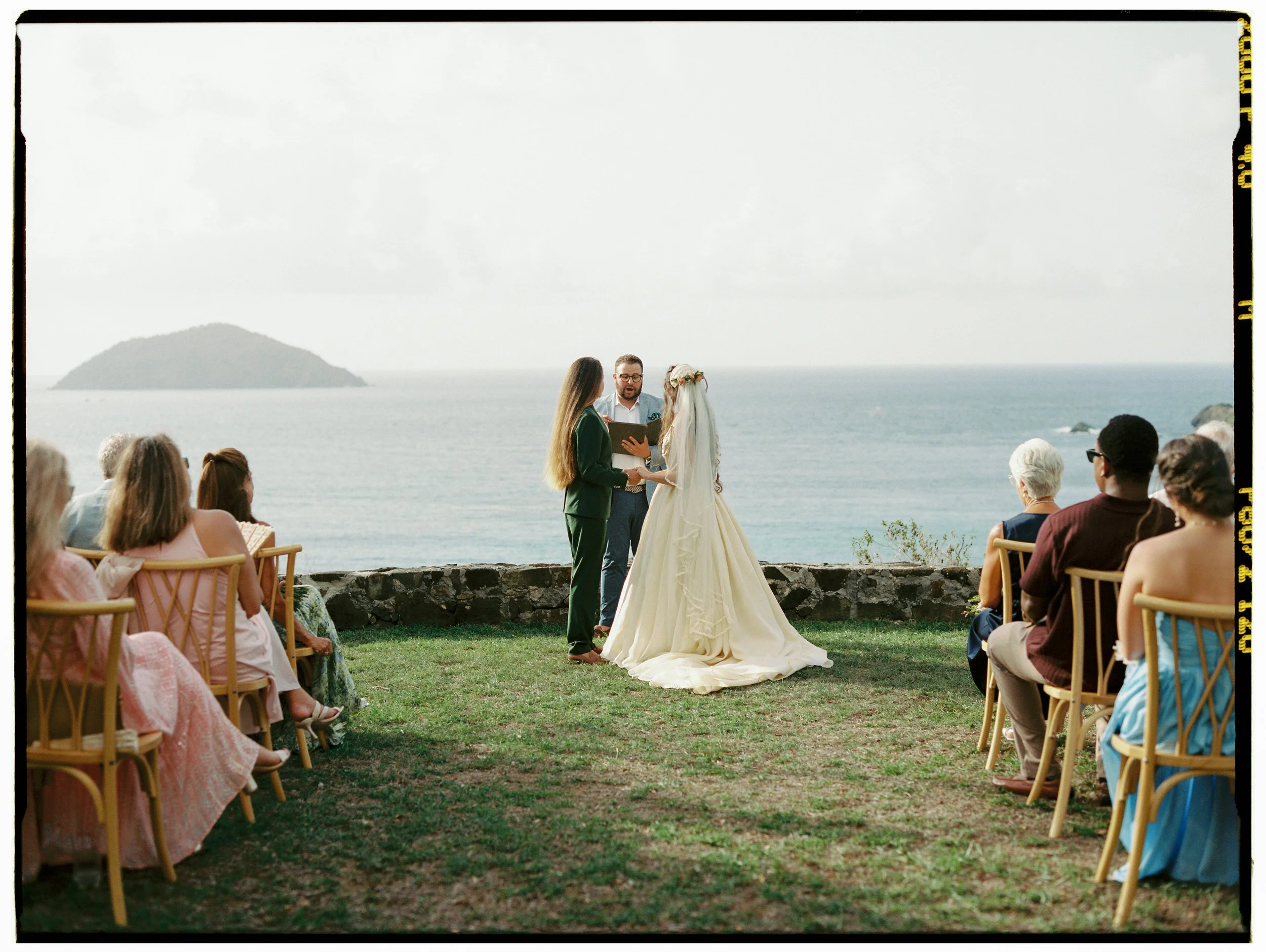 Two brides holding hands during their tropical destination wedding ceremony.