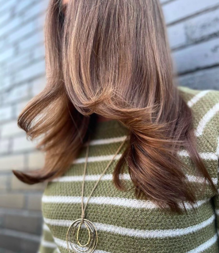 Woman with styled brown hair wearing a striped green sweater and necklace.