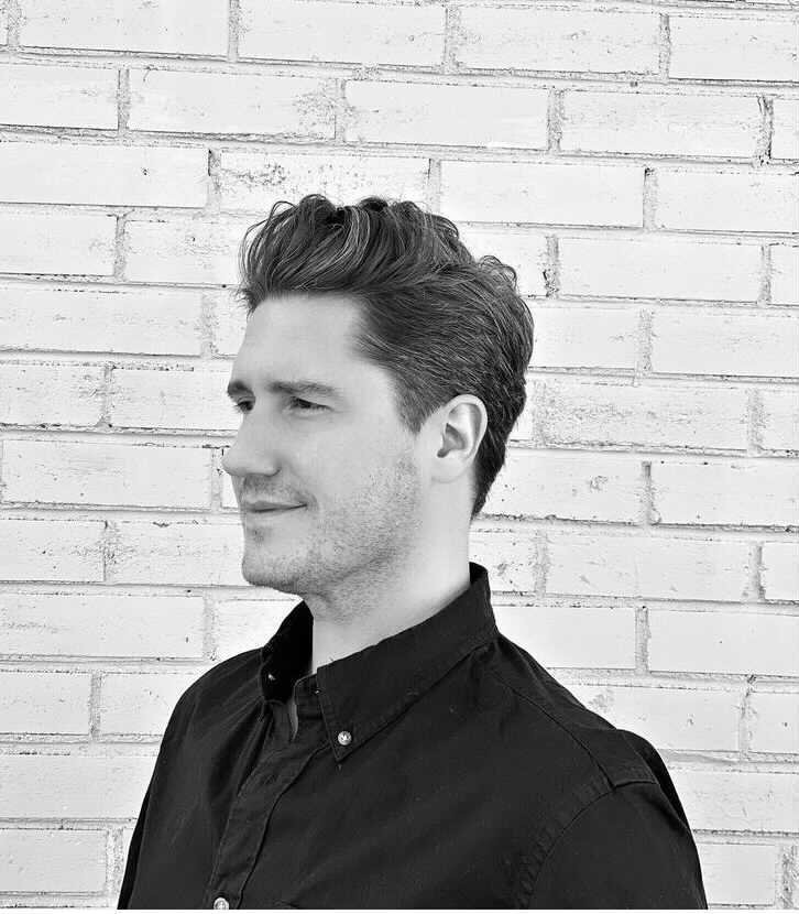 Side view of a man in a black shirt standing against a white brick wall, in black and white.