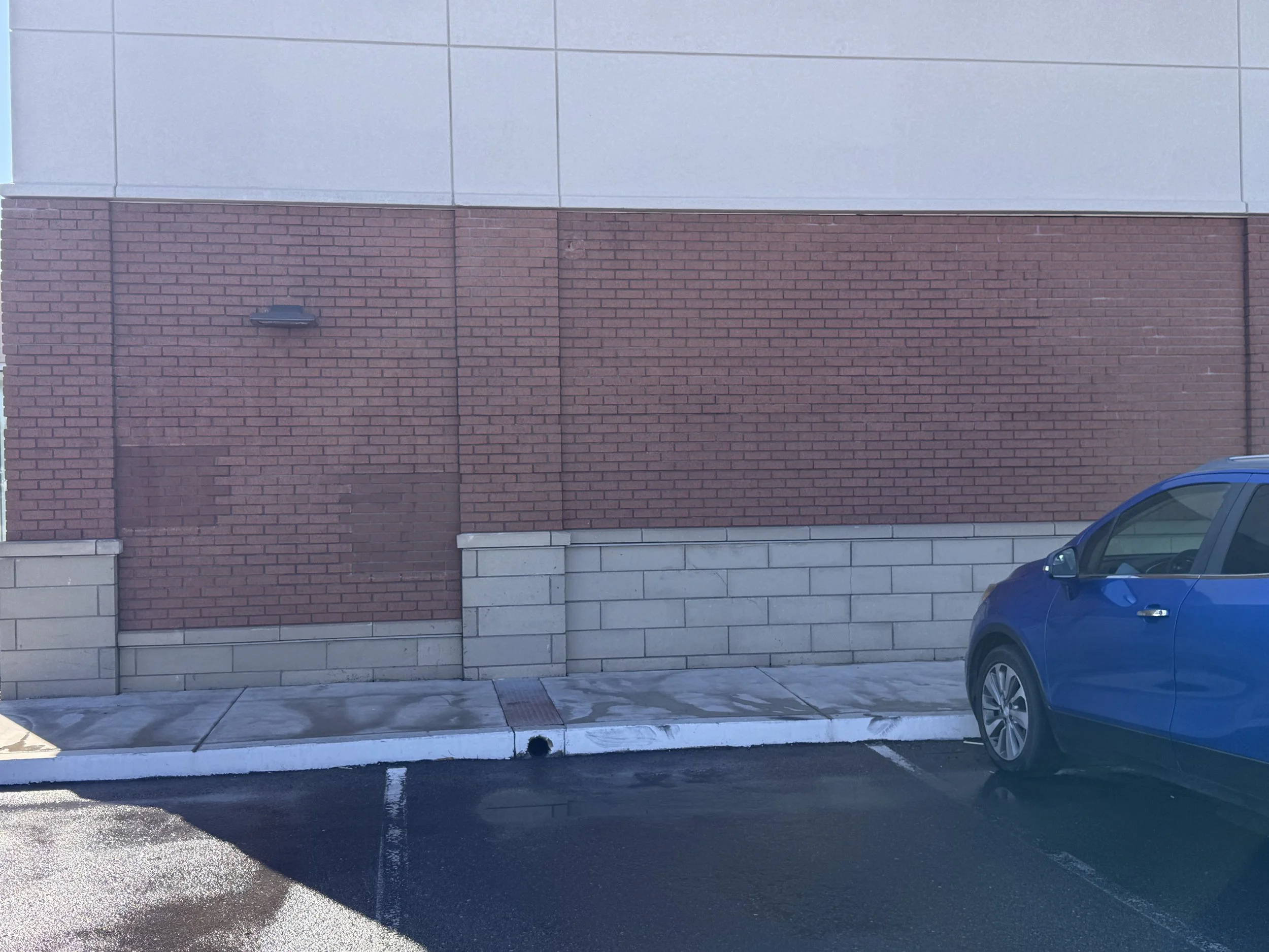 A blue car parked next to a brick and concrete building in a parking lot.