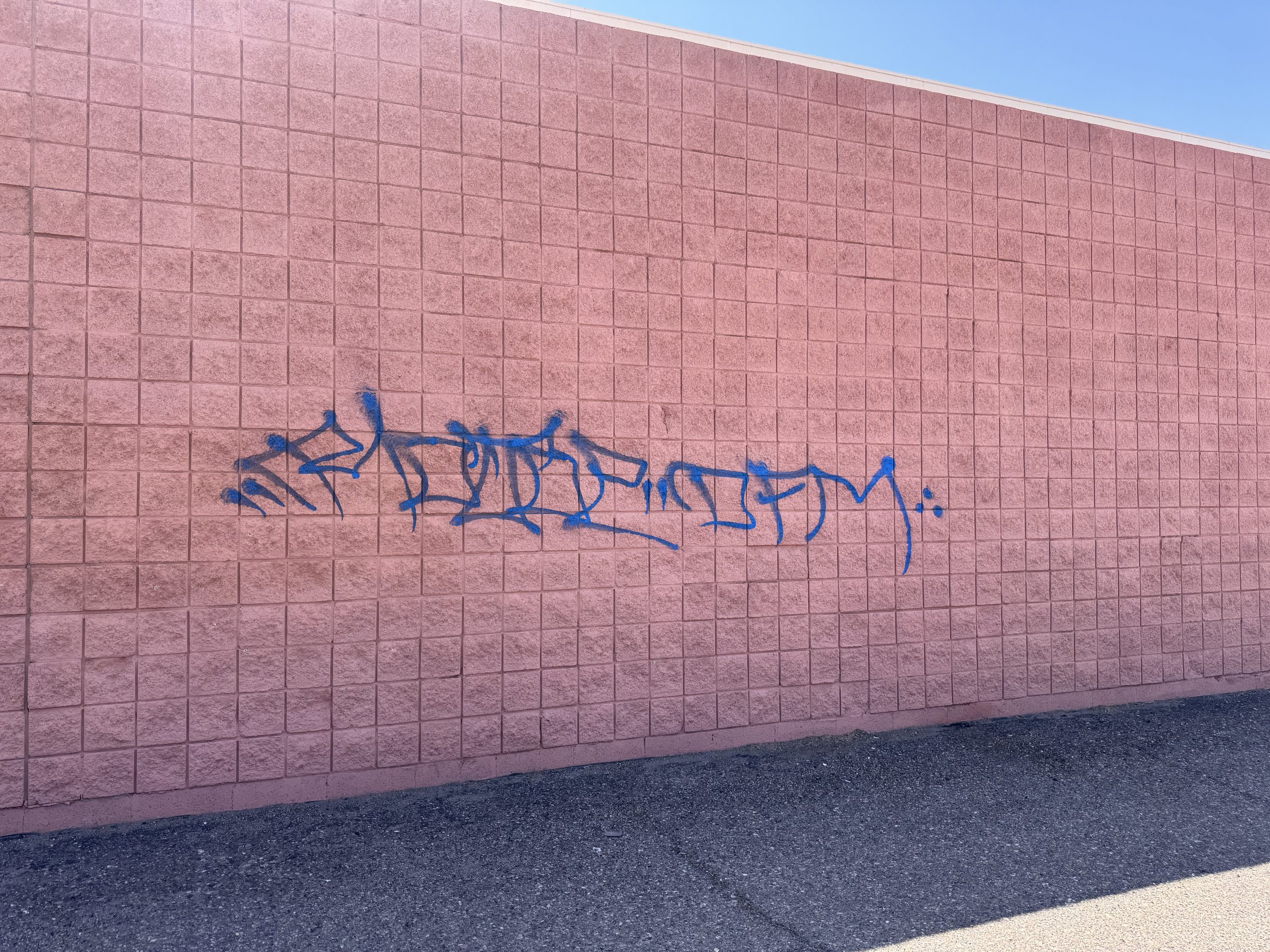 Blue graffiti on a pink brick wall in daylight.
