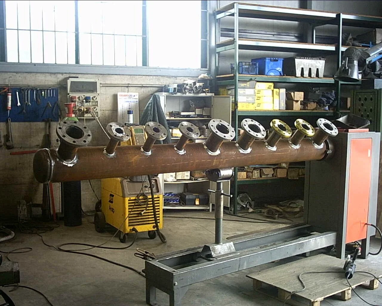 Un grande tubo di legno con flange metalliche attaccate ai bordi, montato su una base metallica in un'officina