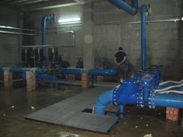 Una sala di impianti idraulici con grandi tubi blu, valvole e una persona che si trova di spalle, in un ambiente industriale