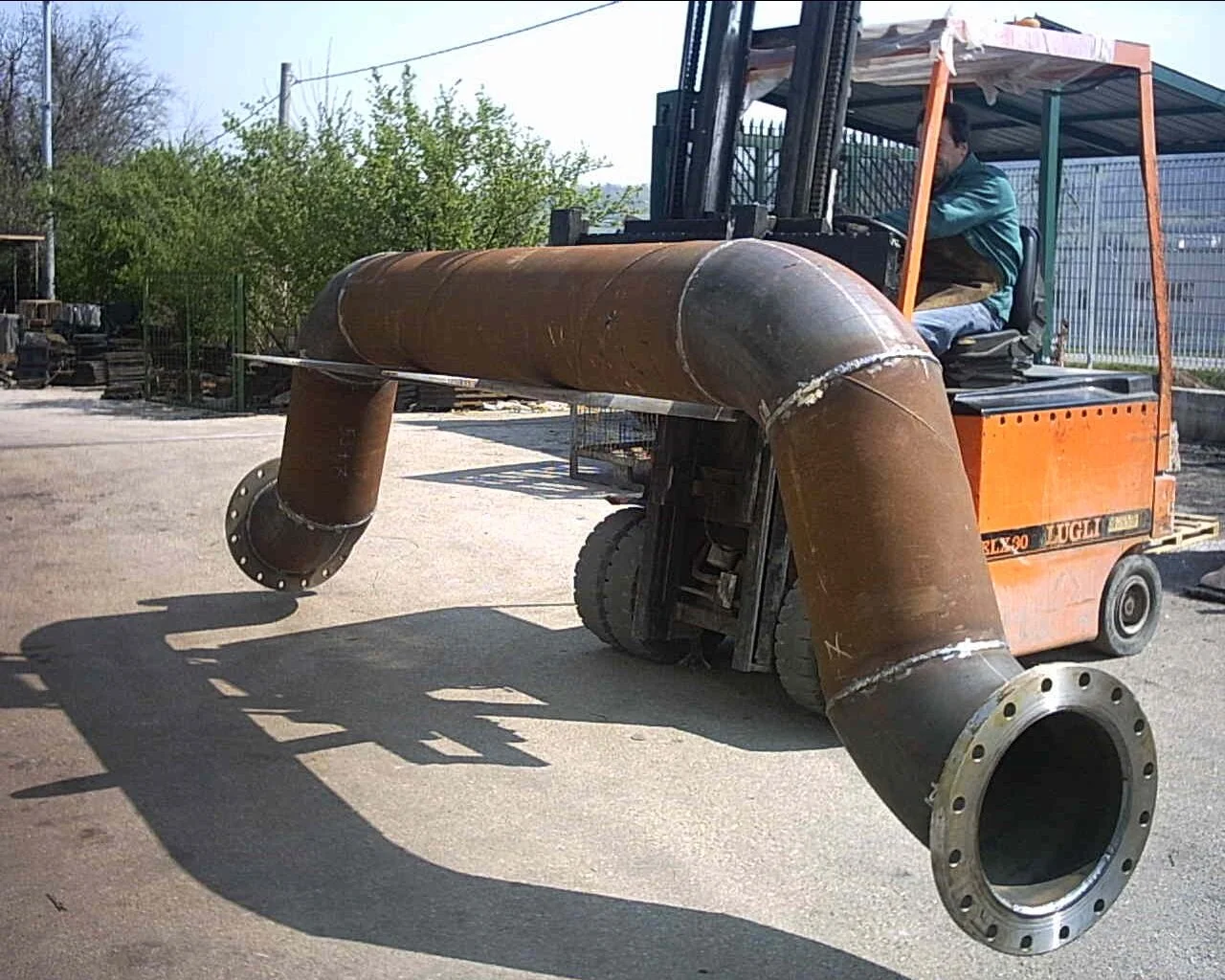 Un carrello elevatore che trasporta una grande tubazione in metallo su un'area all'aperto