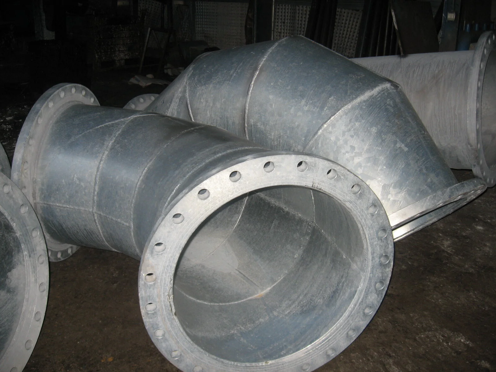 Tubi di metallo spessi con flange forate, probabilmente parti di grandi condotti o impianti industriali.