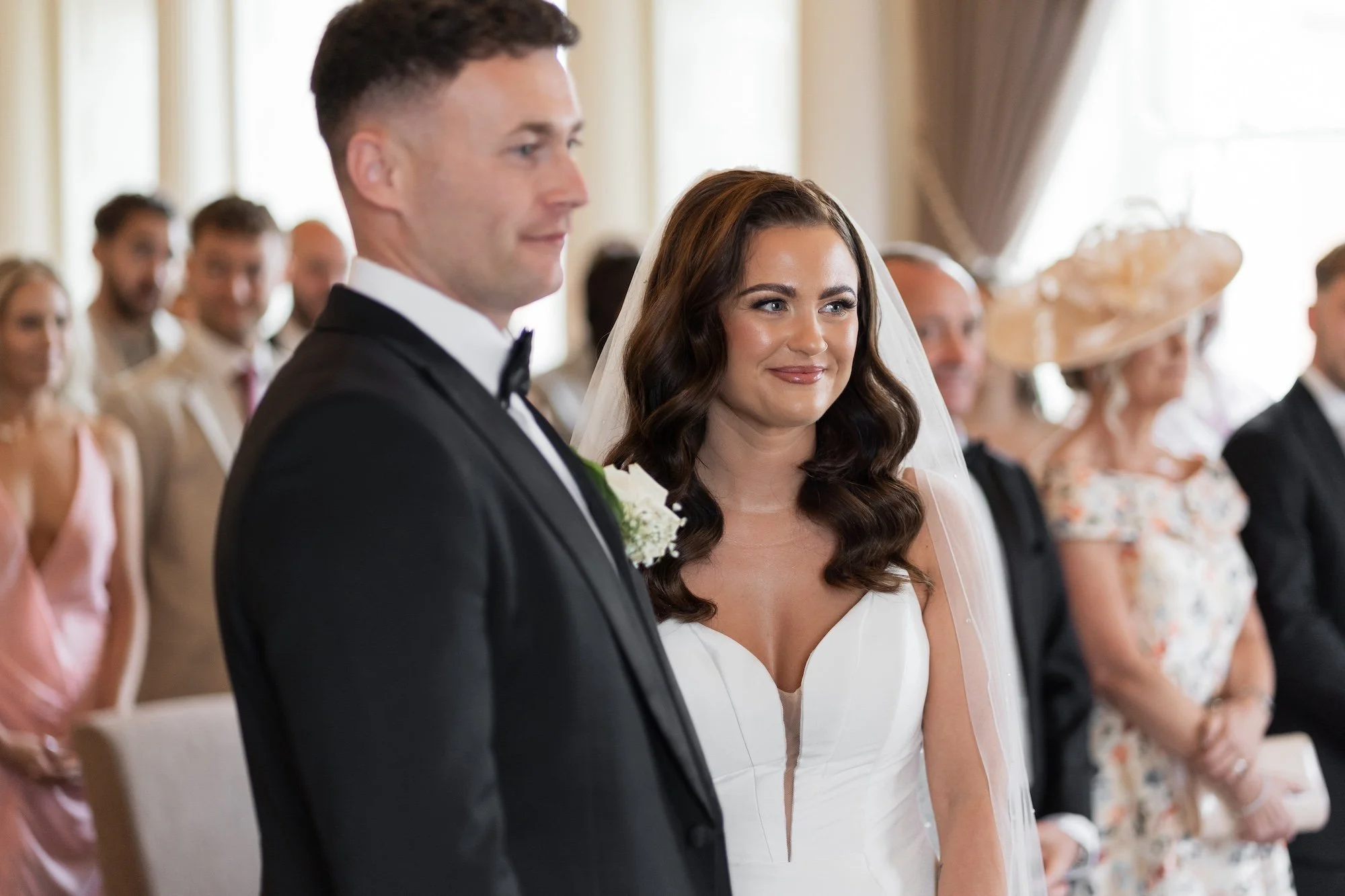 A bride and groom standing during their wedding ceremony, with guests in the background.