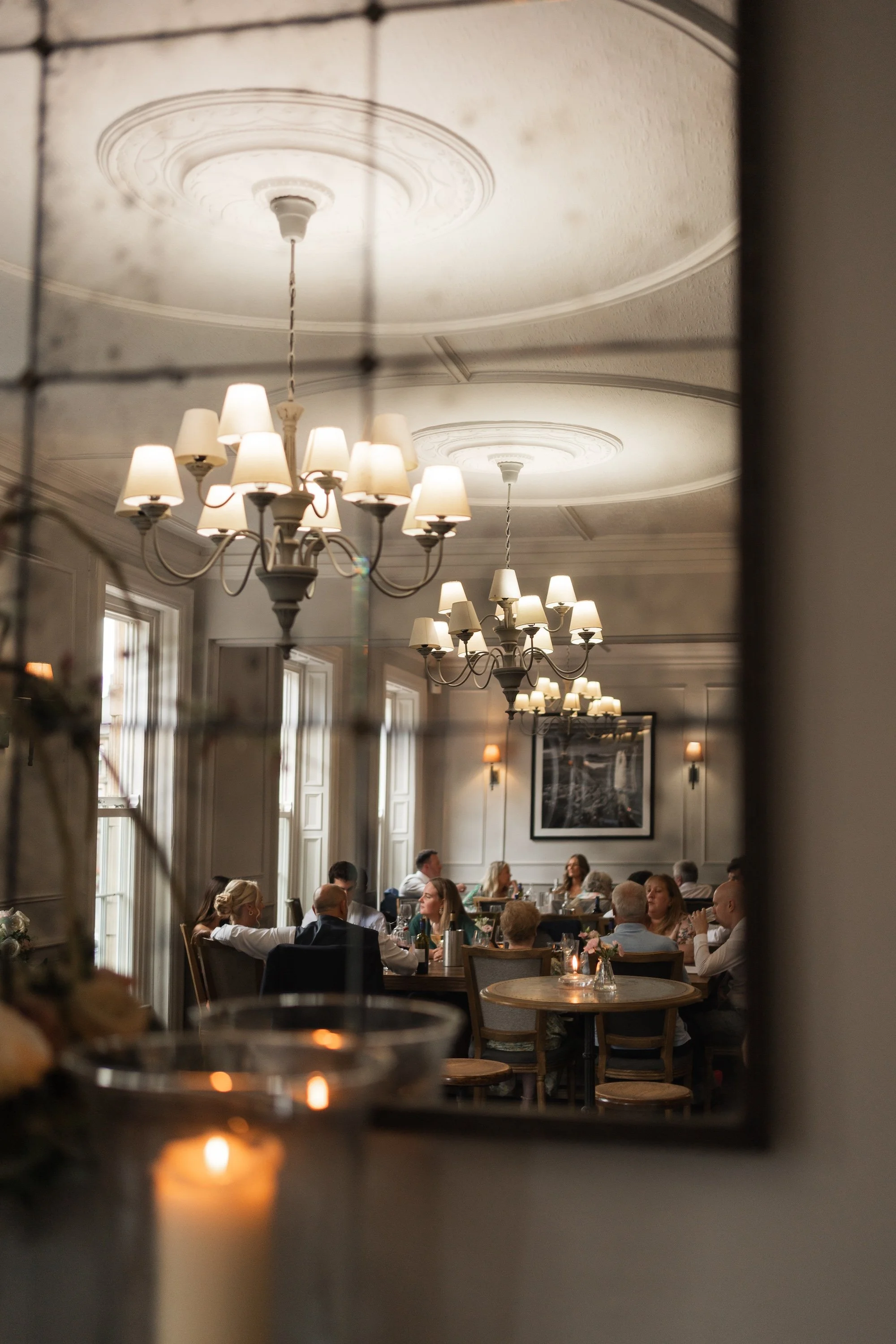 Reflection of a chandelier and dining room with people dining at tables in a mirror. The Beaumont Hotel, Hexham. 