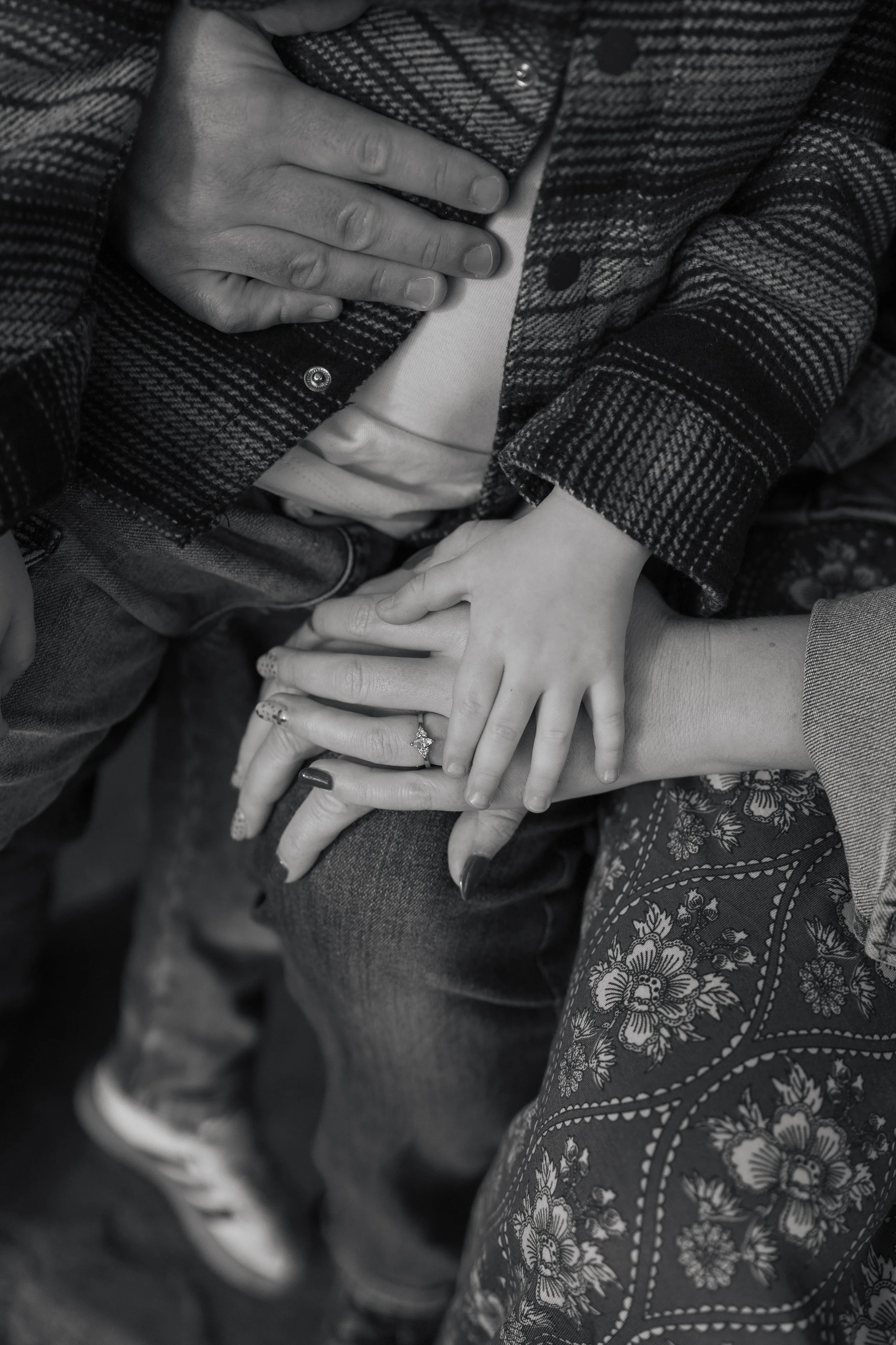 Close-up of multiple hands stacked together, showing a variety of clothing textures and jewelry, including rings and nails.