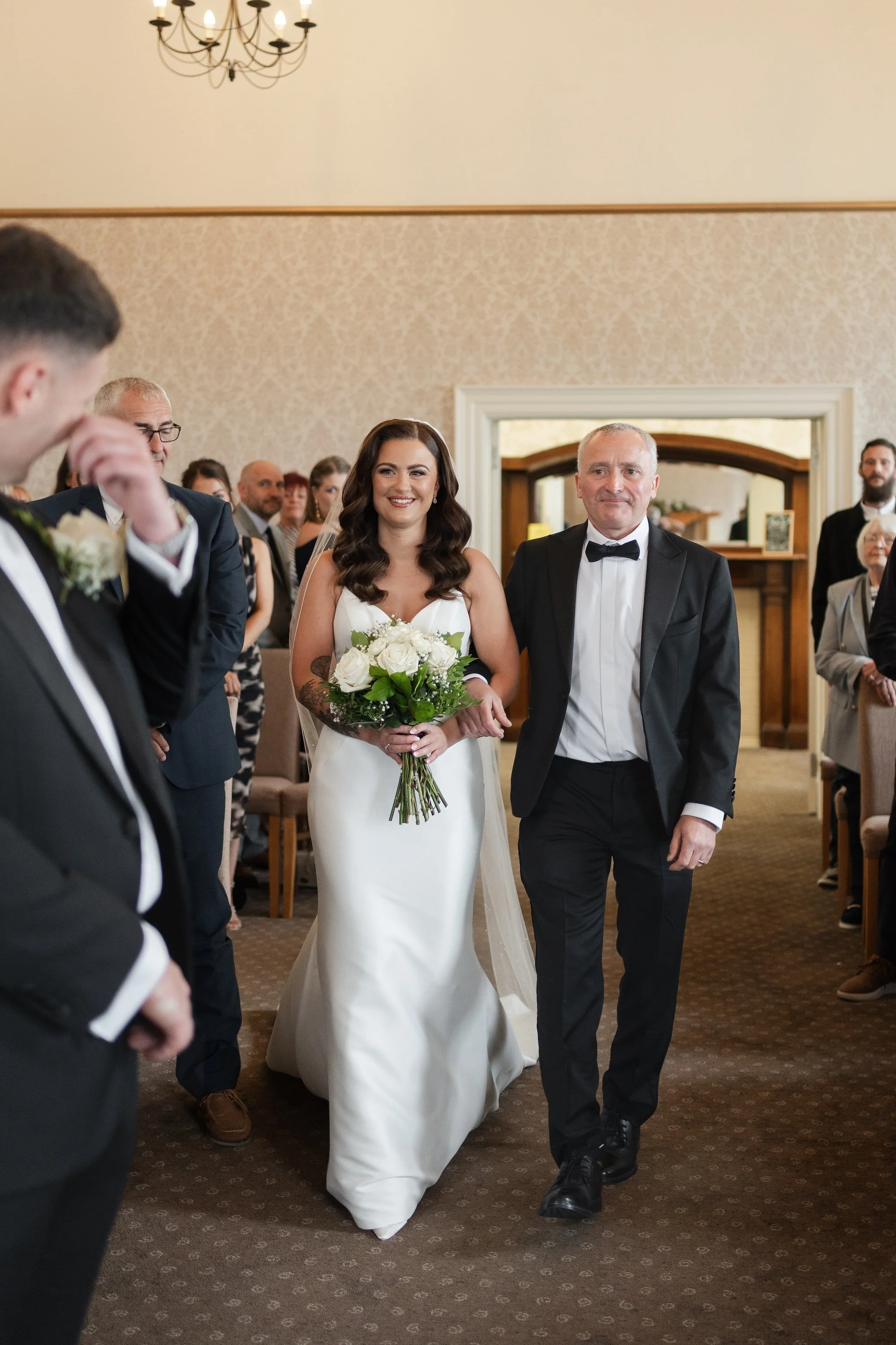 A bride walking down the aisle with her father at a wedding ceremony in a church, surrounded by guests.