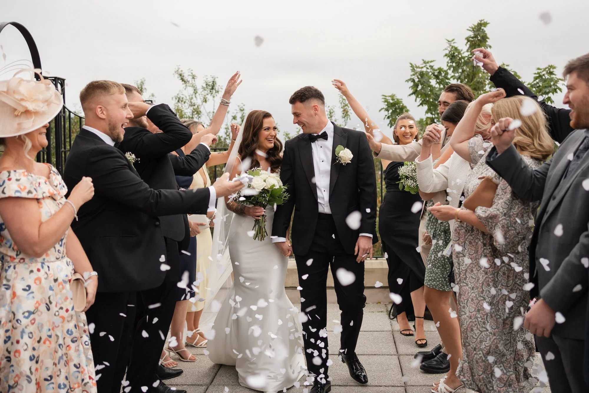 Bride and groom walking hand in hand while friends and family celebrate with confetti at an outdoor wedding. North Tyneside Registry Office. 