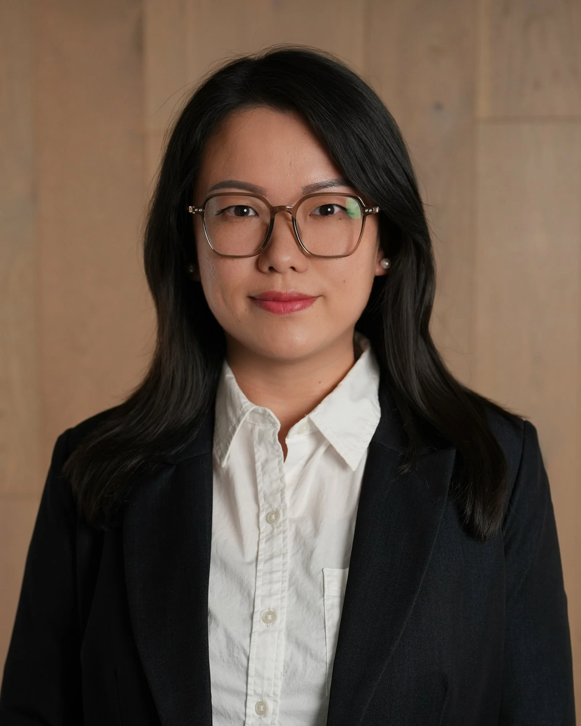 Headshot of Ting Yang, with straight, shoulder-length dark hair, brown glasses, fair skin, and wearing a white shirt and black blazer.