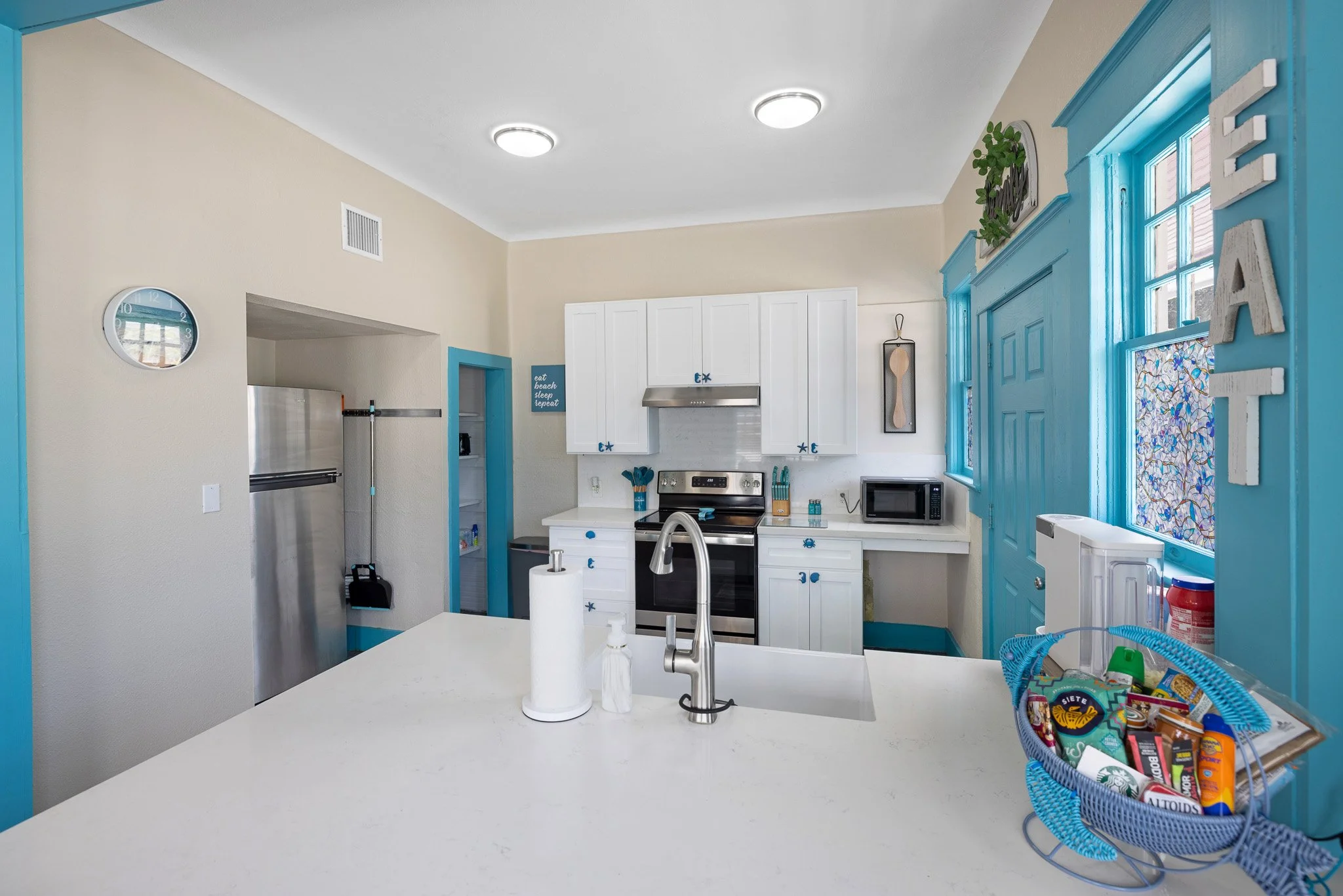 Kitchen with white cabinets, stainless steel stove, microwave, blue accents, and a white island counter.