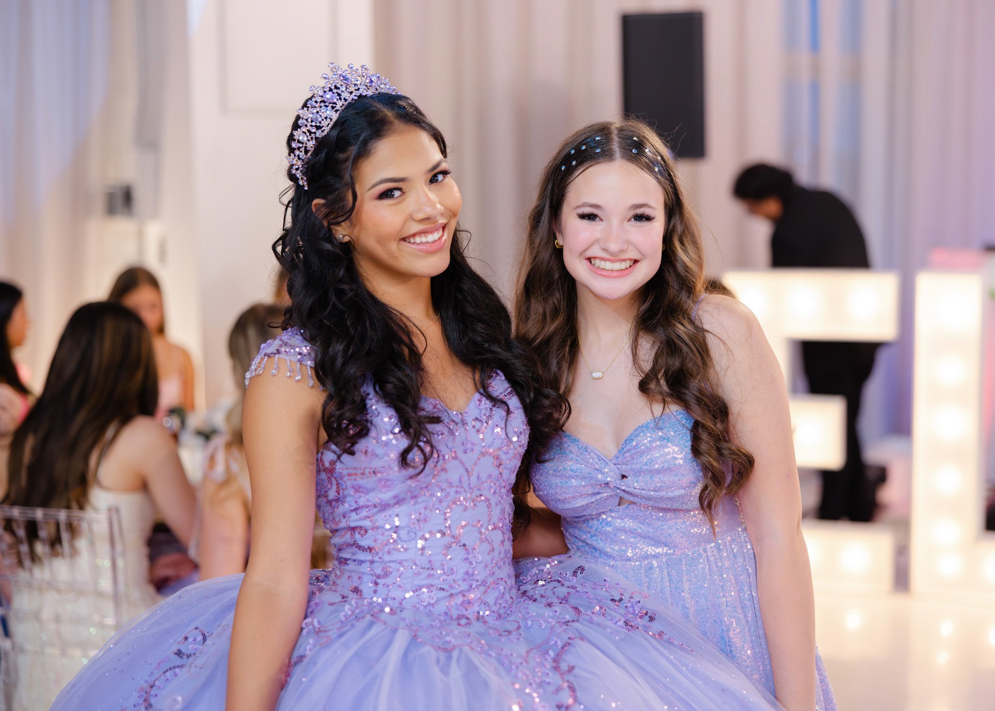 Two young women dressed in lavender ball gowns at a formal event, smiling at the camera.