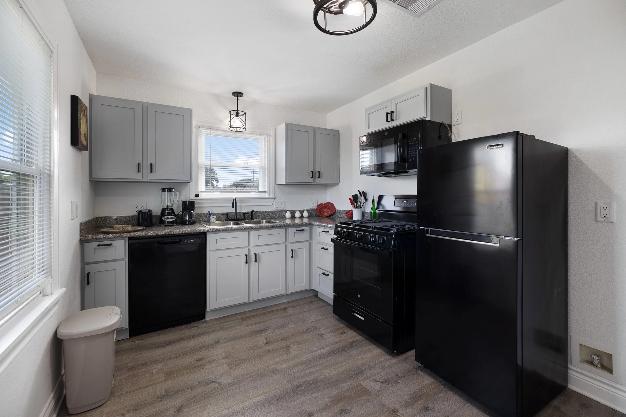 Modern kitchen with gray cabinets, black appliances, a window above the sink, and light wood flooring.