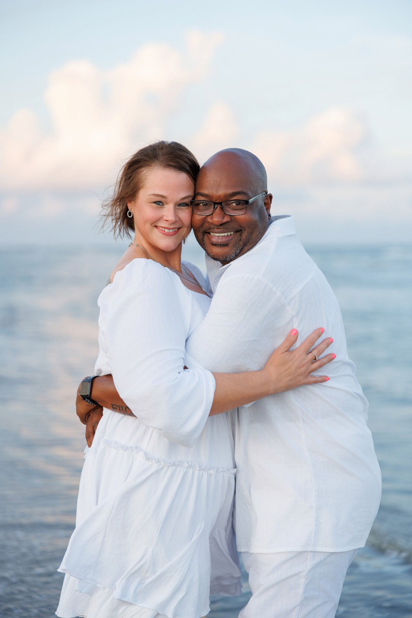 A happy couple hugging each other on the beach with the ocean and sky in the background.
