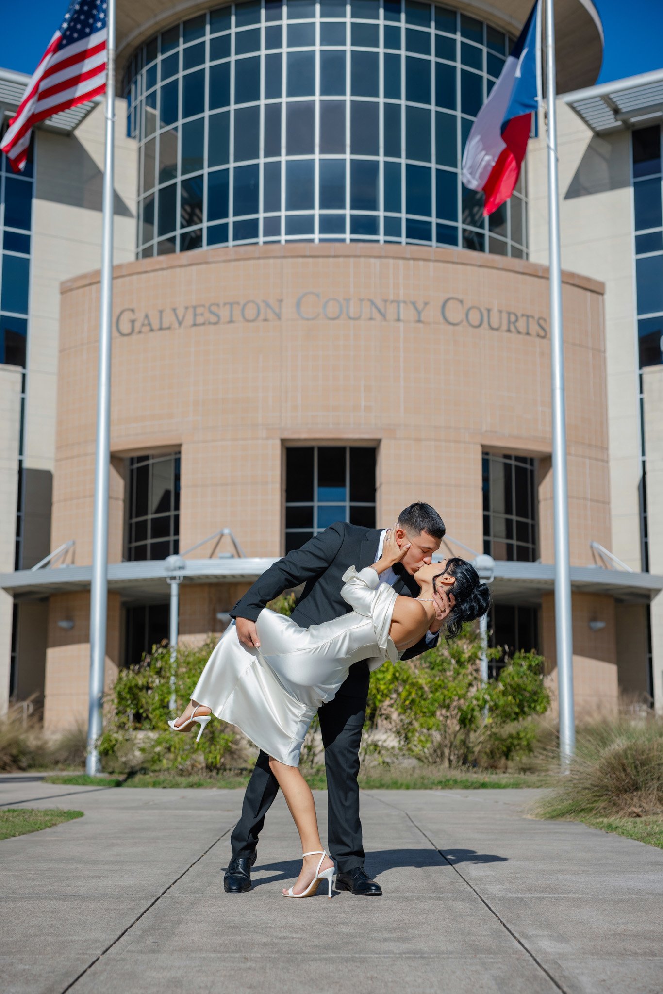 A couple dancing outside the Galveston County Courthouse, with the man dipping the woman for a kiss as the flags flutter in the wind.