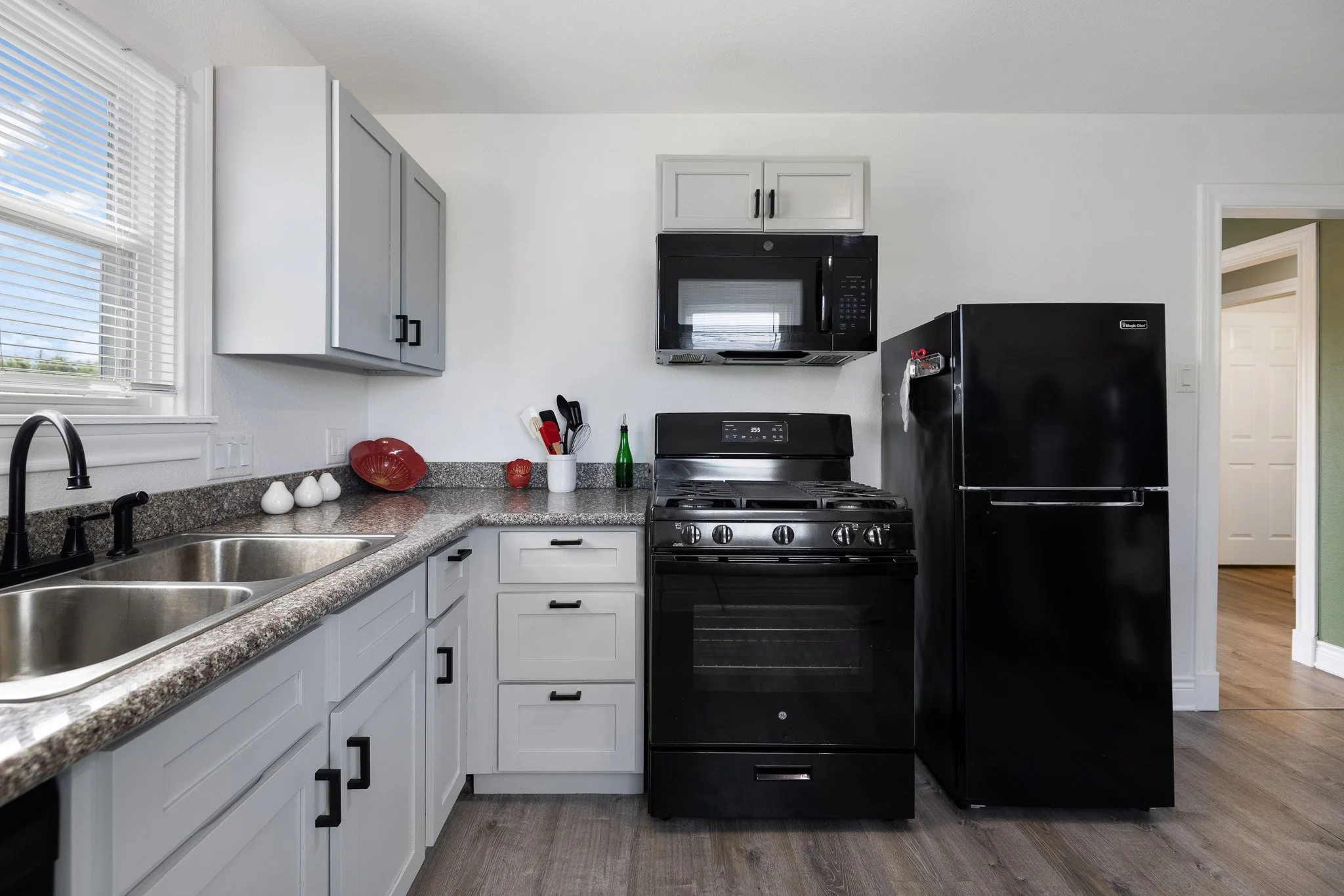 Kitchen with white cabinets, granite countertops, black appliances including a refrigerator, stove, and microwave, and a window with blinds.