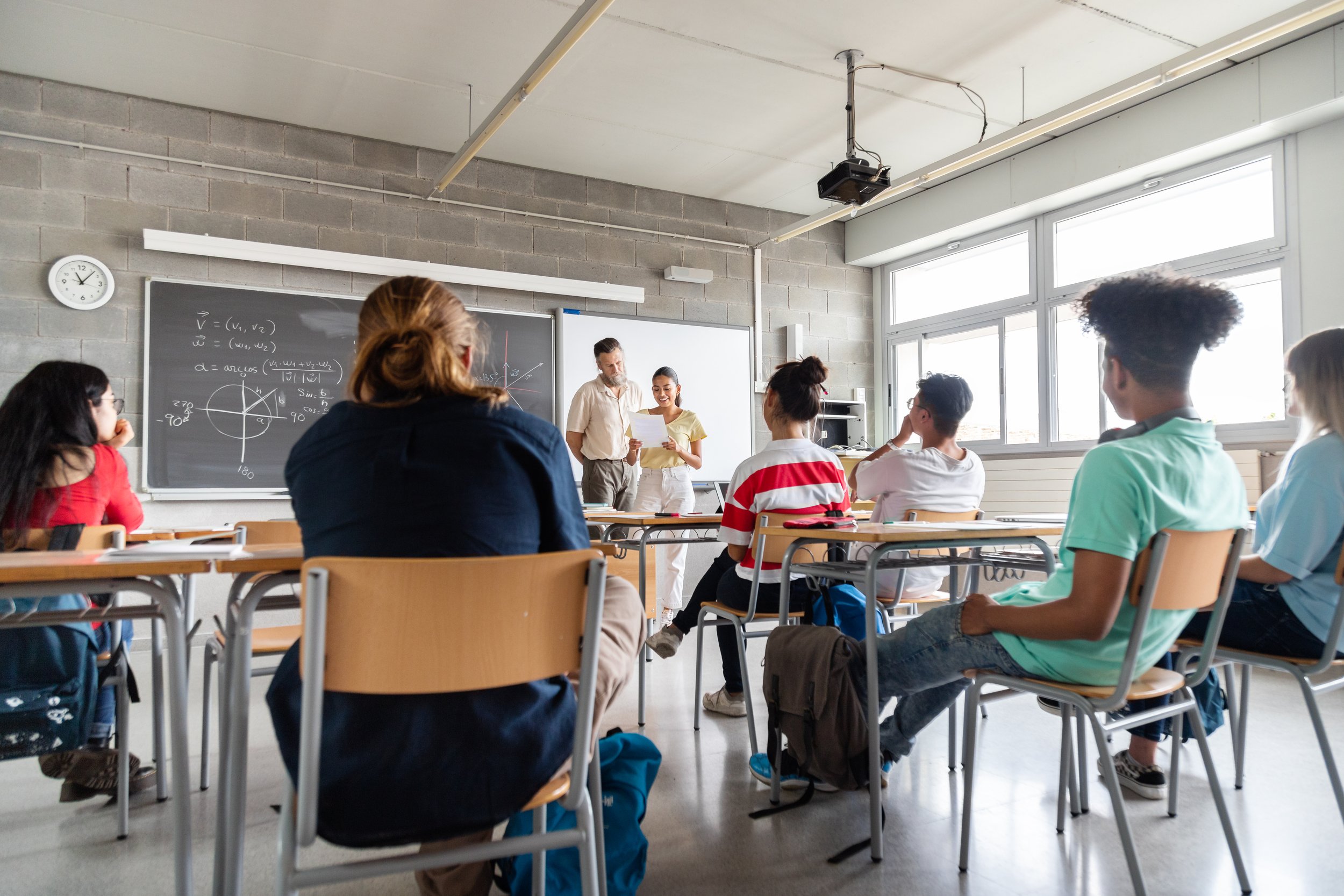 Classroom with students sitting at desks and a teacher standing at the front.