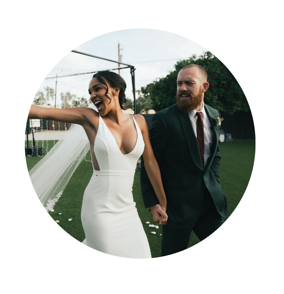 A bride and groom holding hands and smiling outdoors during their wedding ceremony