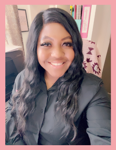 A woman with long black wavy hair smiling in an office setting with bookshelves and a desk.