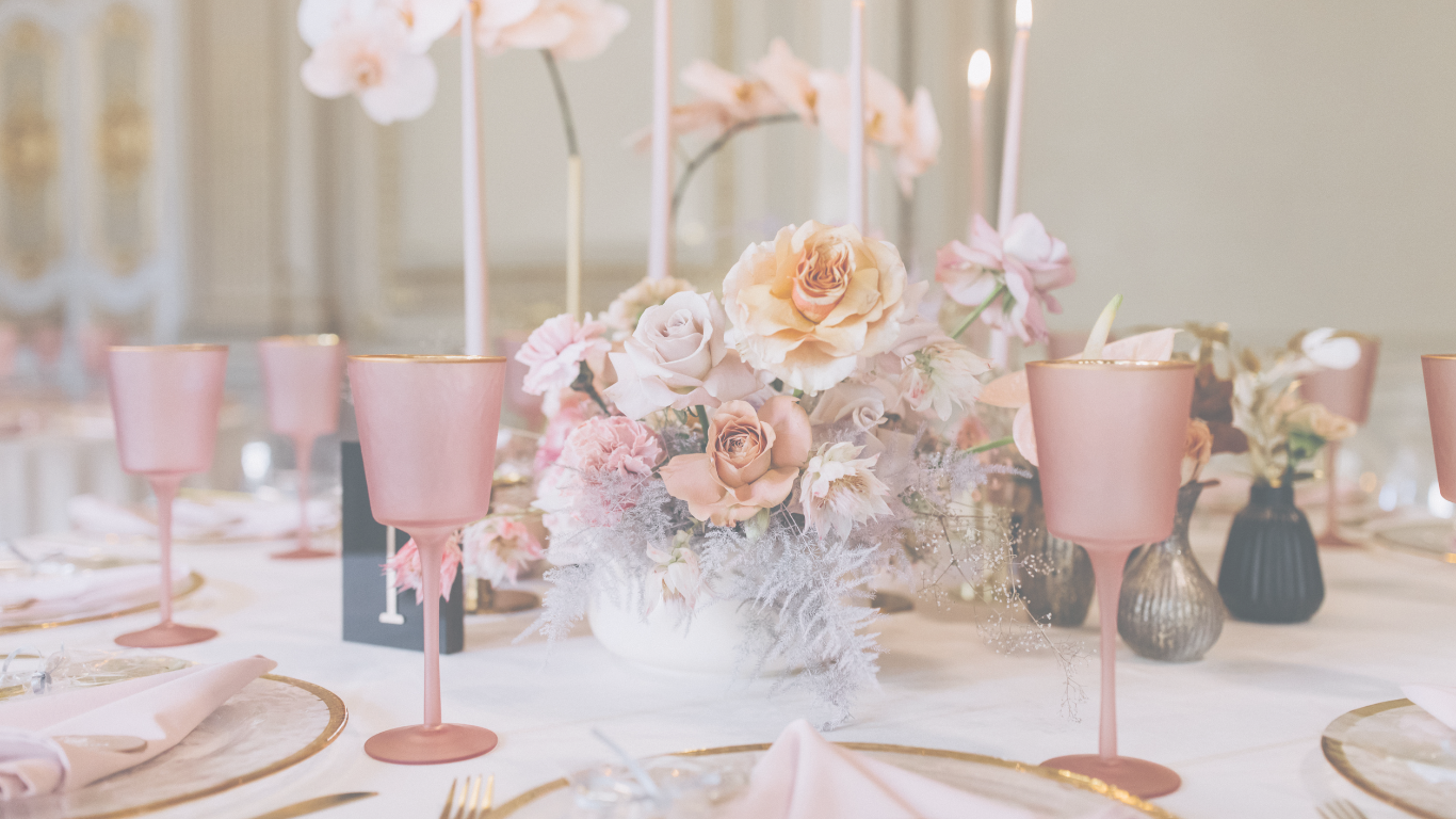 A table decorated with a floral centerpiece, pink glasses, and elegant table settings for a special occasion.