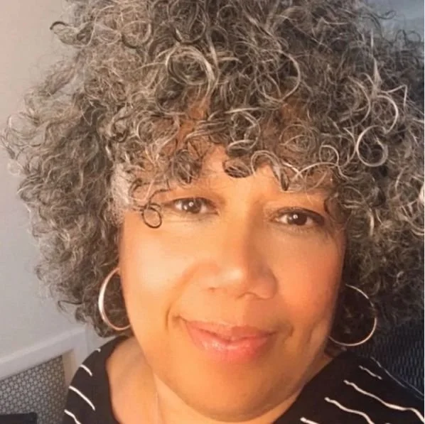 Person with curly gray hair and hoop earrings smiling.