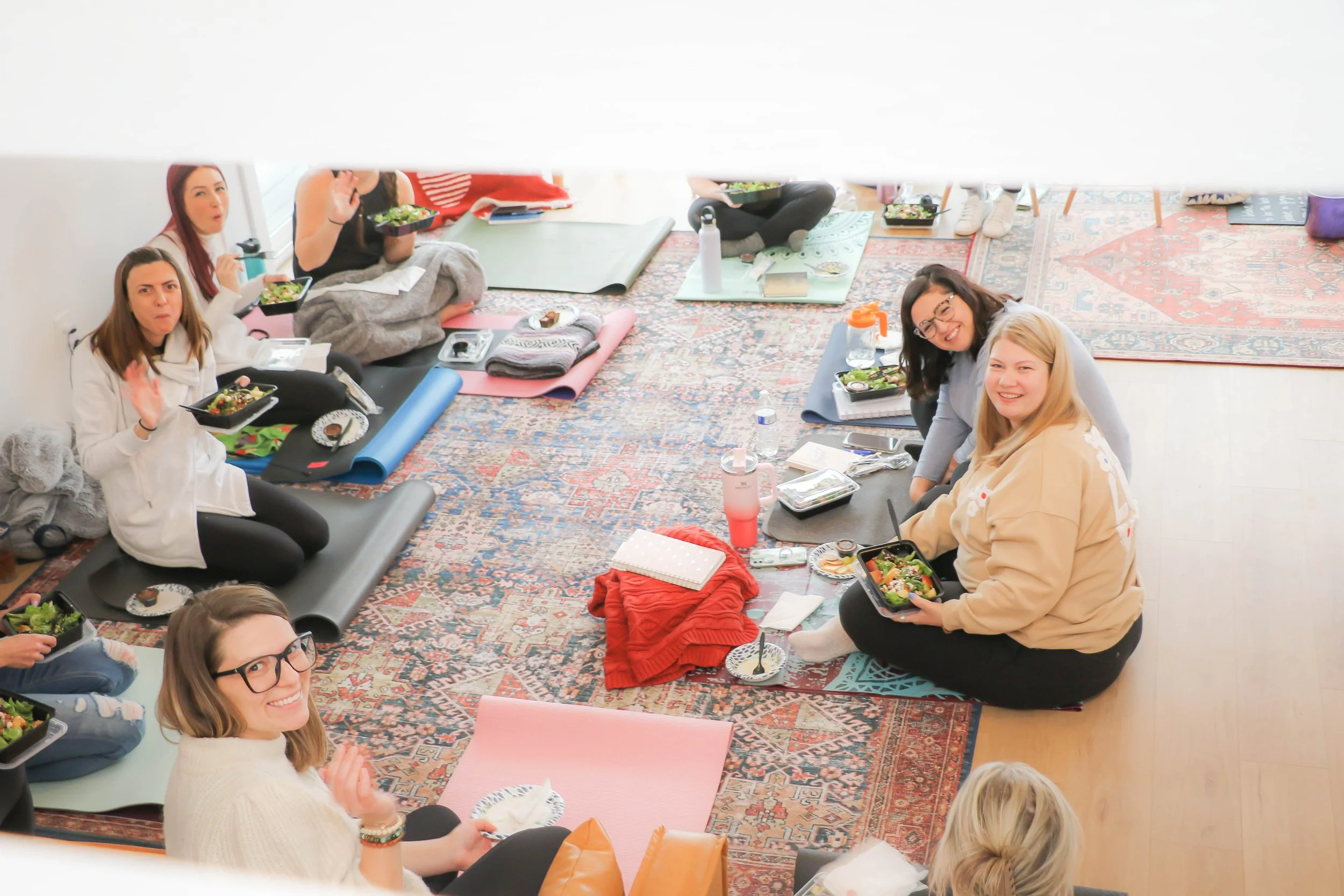 Group of people sitting on yoga mats eating together indoors.