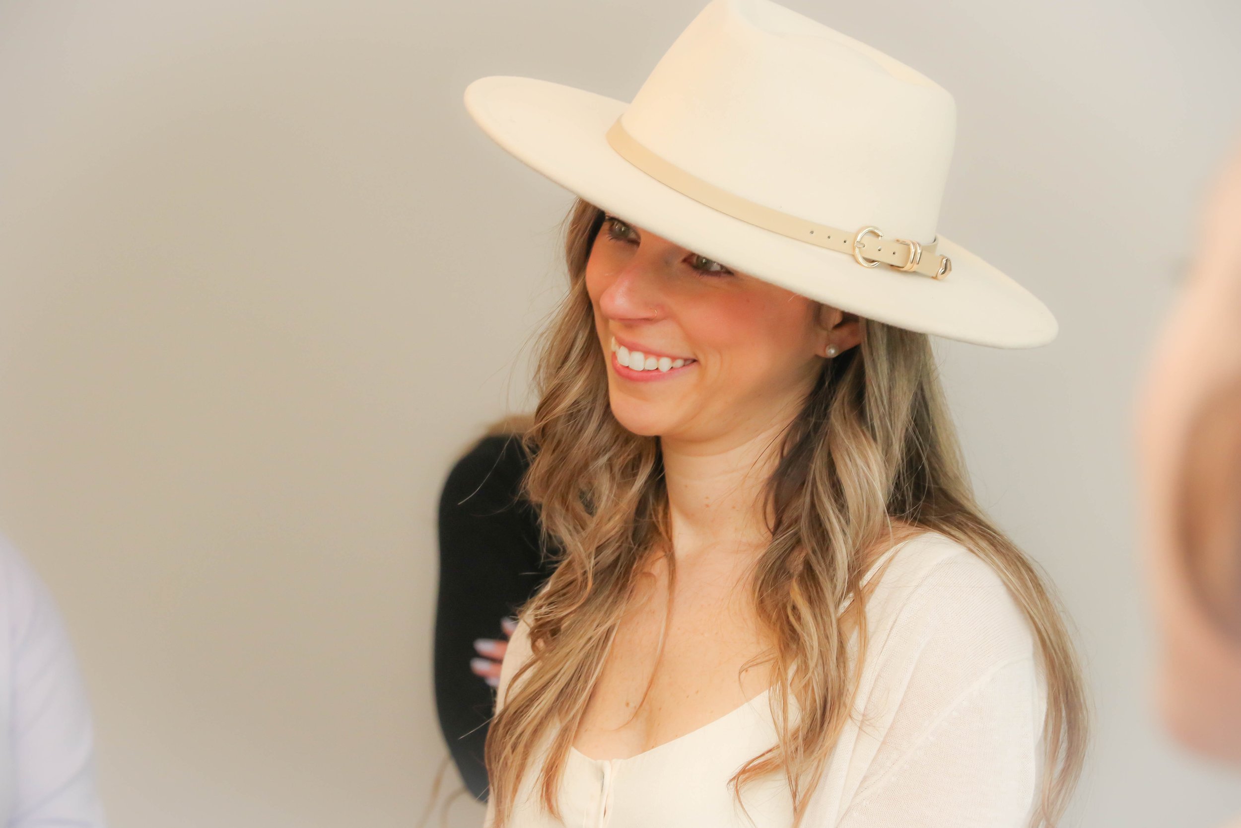 Woman wearing a white wide-brimmed hat and smiling.