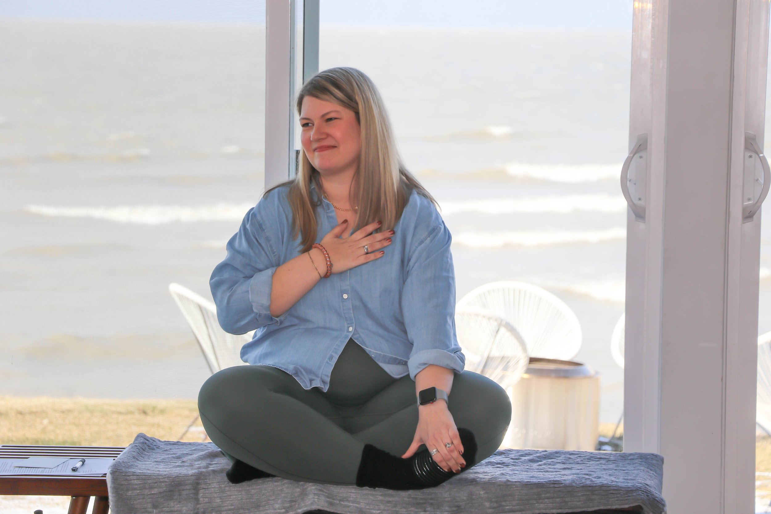 Woman meditating indoors by a window with a view of the ocean.