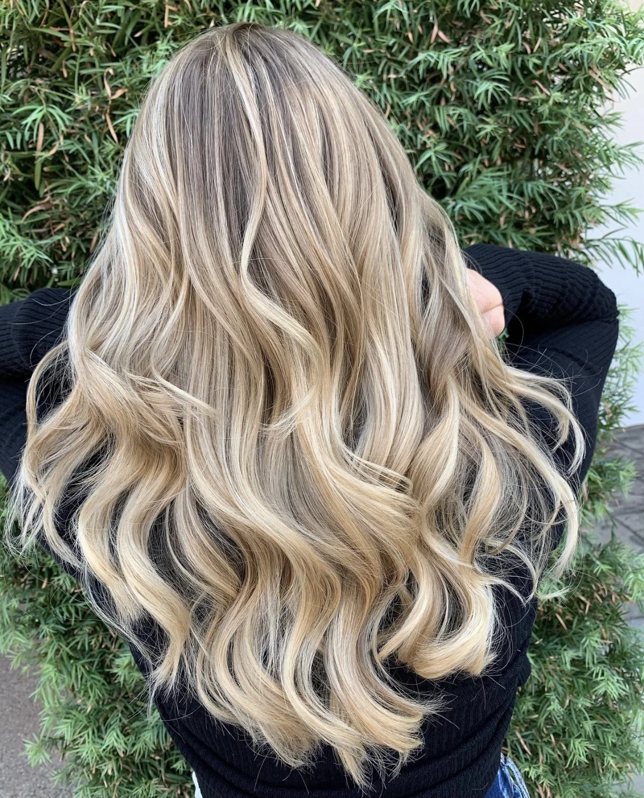 Long blonde highlights with darker roots and cascading waves, viewed from behind.