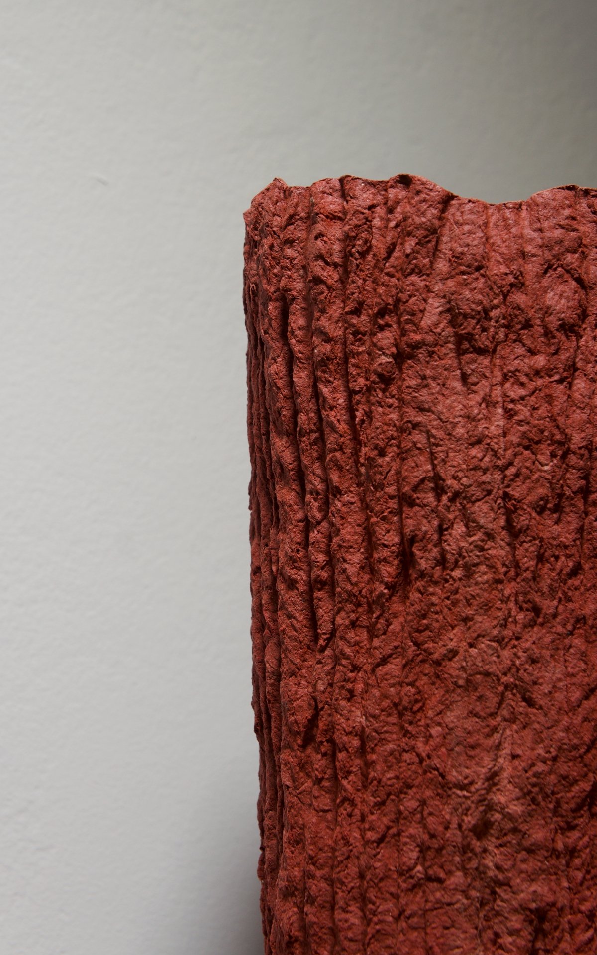 Textured red sculpture resembling bark against a white background.