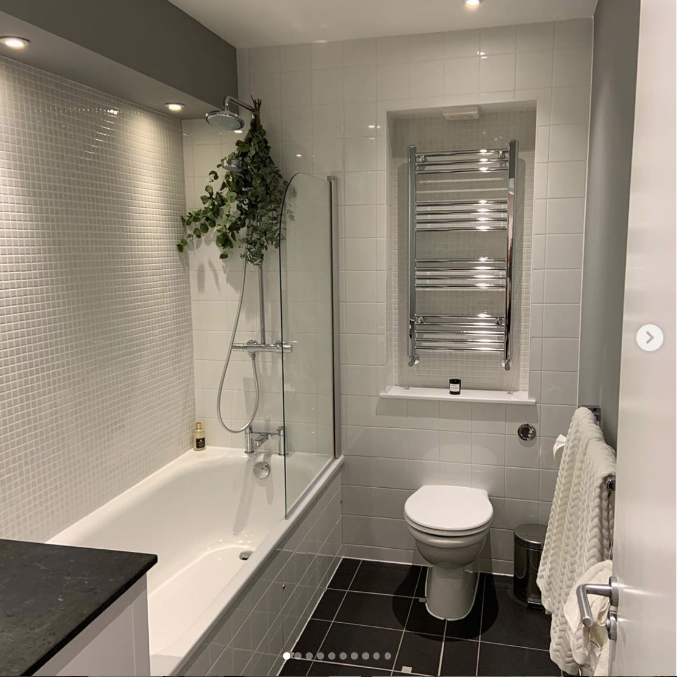 Modern bathroom with a shower and bathtub, white tiled walls, a toilet, a heated towel rack, a small window, and a towel hanging on a towel bar.