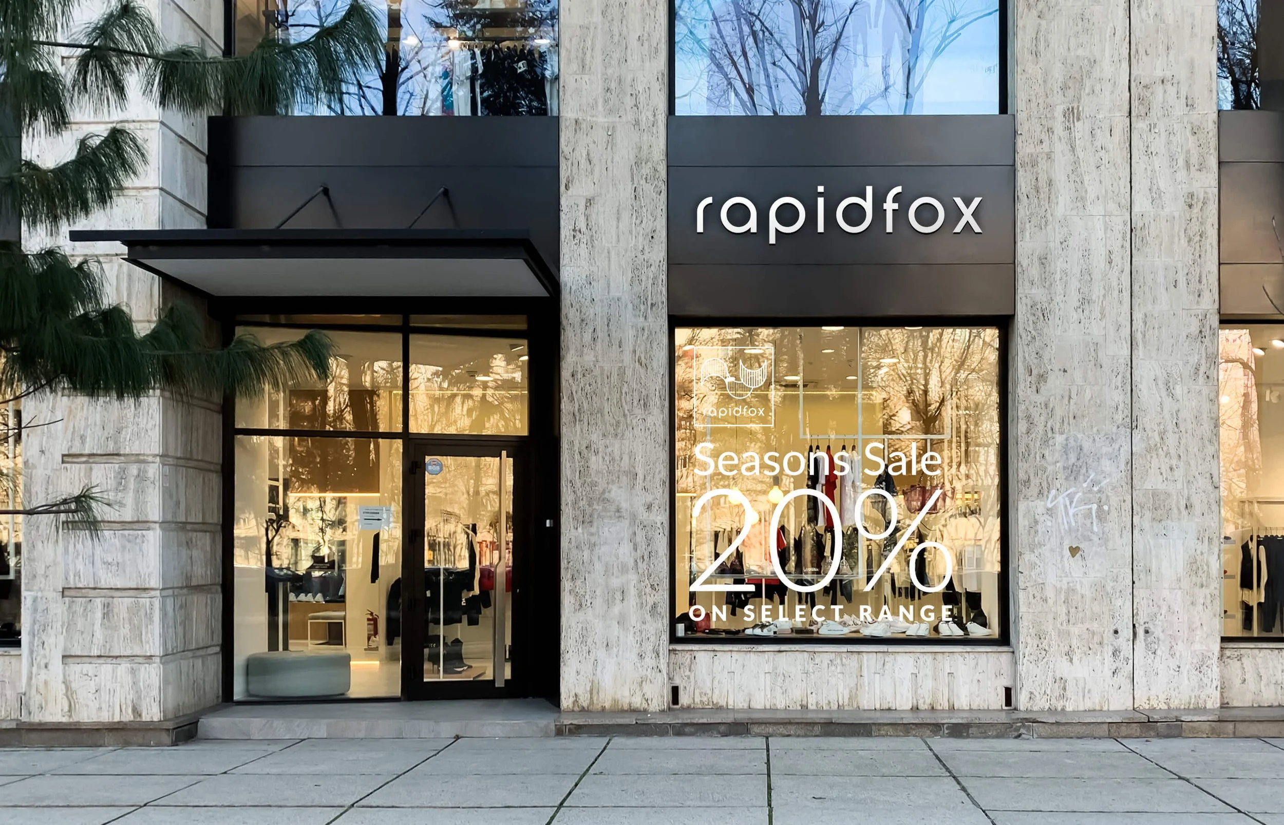 Facade of a clothing store named Rapidfox with large windows displaying a seasonal sale of 20% off on select items, with the store's signage visible above the entrance.